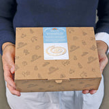 Jemand hält eine Grimms-Kartonverpackung mit der Freies Spiel: Festtagsspirale natur, einer aus geöltem Erlenholz gefertigten Spirale mit 8 Elementen und 24 Kerzenhaltern, ideal für festliche Dekorationen.