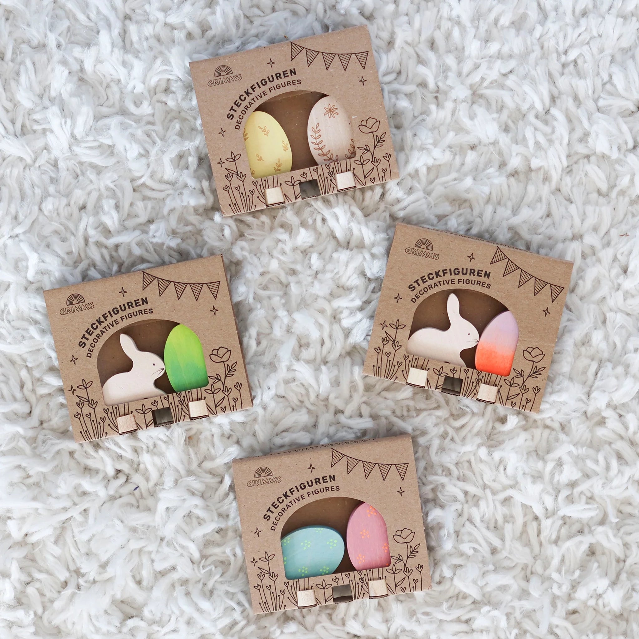 Vier identische Kartonboxen zeigen das Steckfigur: Osterset Batik Orange von GRIMM'S, mit einem Holzhasen und buntem Ei, handbemalt aus Lindenholz, ideal zur Osterdekoration, passend für nachhaltige, moderne Ästhetik.
