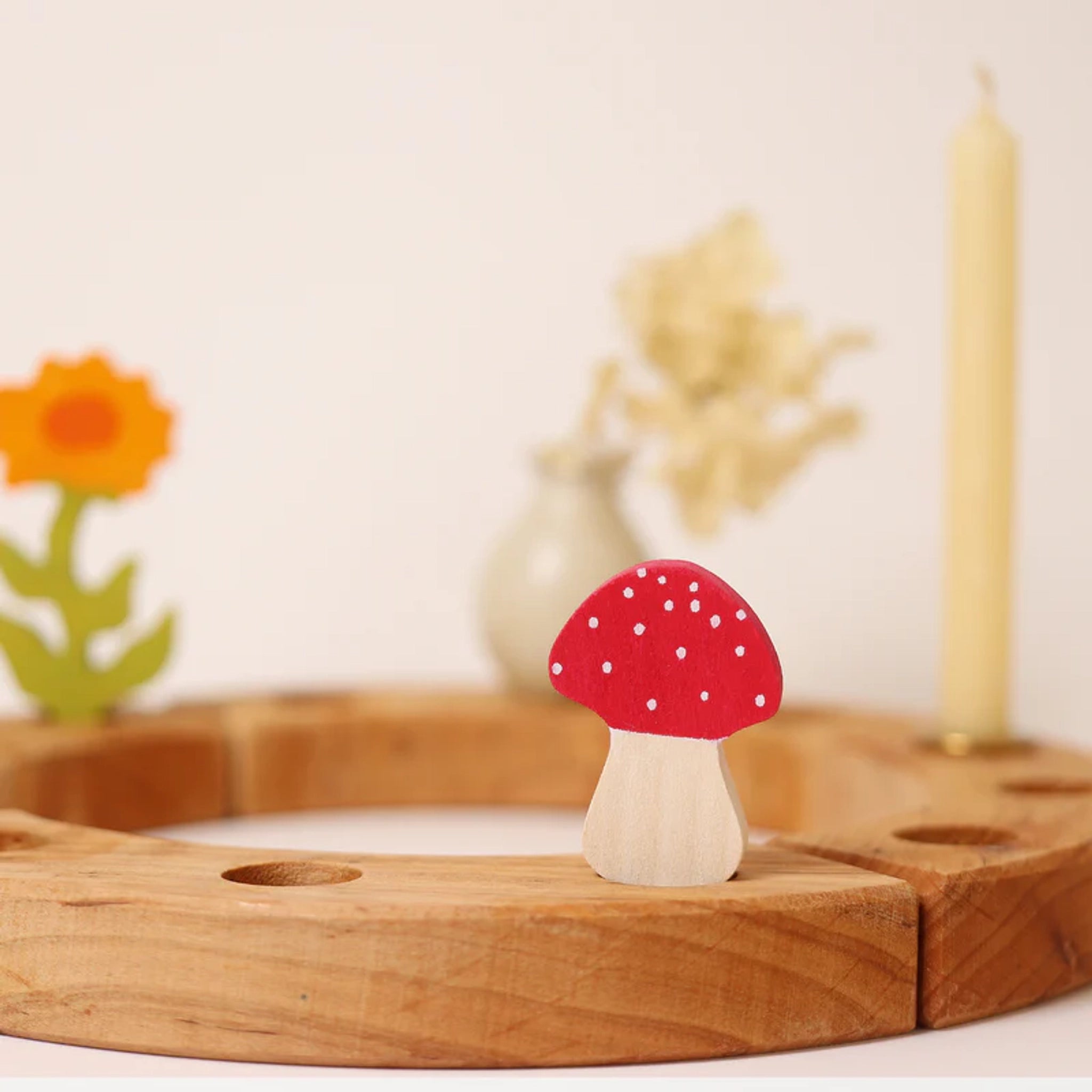 Steckfigur: Fliegenpilz, ein handbemalter Holzpilz mit rotem Hut und weißen Punkten, sitzt auf einem Holzkranz. Ergänzt durch eine gelbe Kerze, Trockenblumen und eine stilisierte Holzblume.
