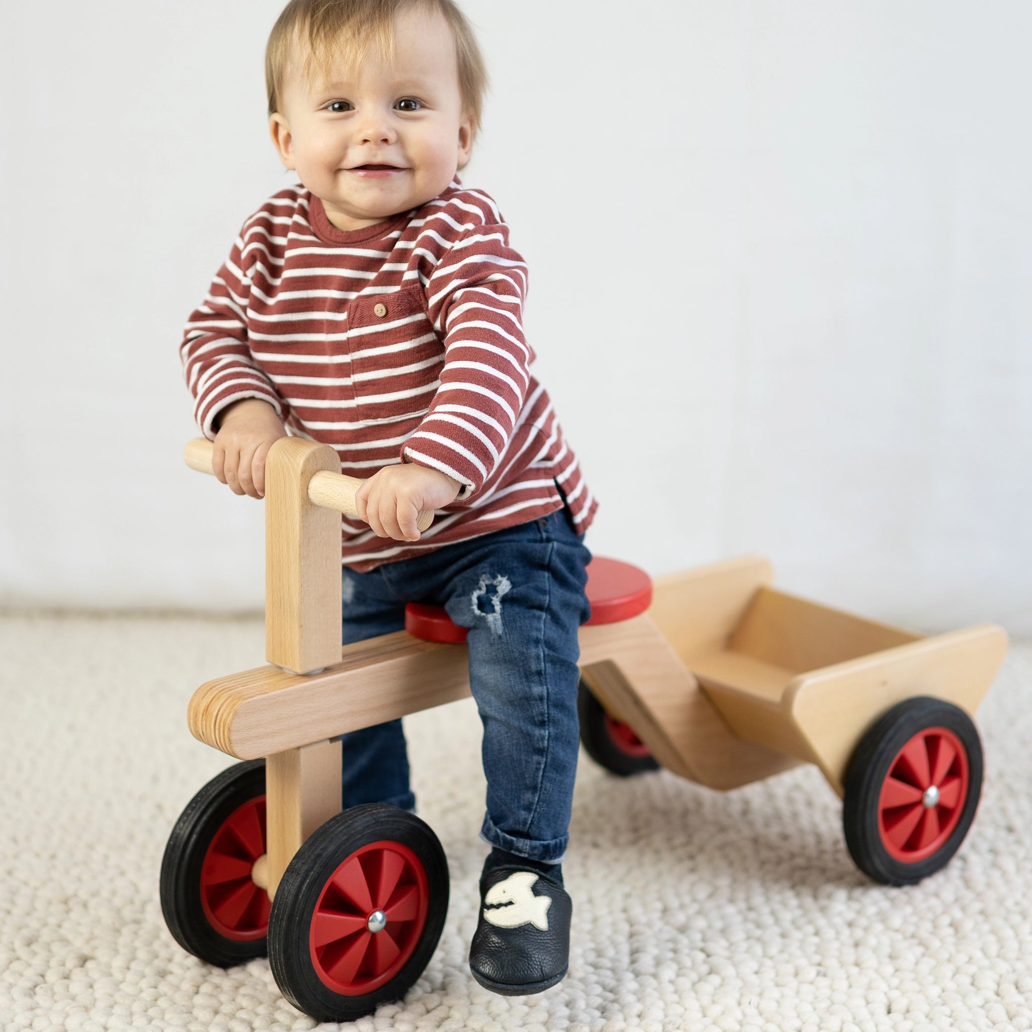 Ein Baby fährt auf einem Rutschauto aus massivem Buchenholz mit hochwertigen Gummirädern, ideal für drinnen. Hergestellt in einer geschützten Werkstätte in Vorarlberg, Österreich.