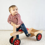 Ein Baby sitzt auf einem Rutschauto aus massivem Buchenholz mit hochwertigen Gummirädern, ideal für den Innenbereich, hergestellt in einer geschützten Werkstätte in Vorarlberg, Österreich.