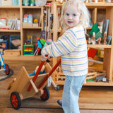 Kind schiebt Schubkarre aus massivem Buchenholz mit Gummimantelrädern, ideal für kleine Handwerker. Hergestellt in Vorarlberg, Österreich, von waelderspielzeug, bietet es nachhaltigen Spielspaß.