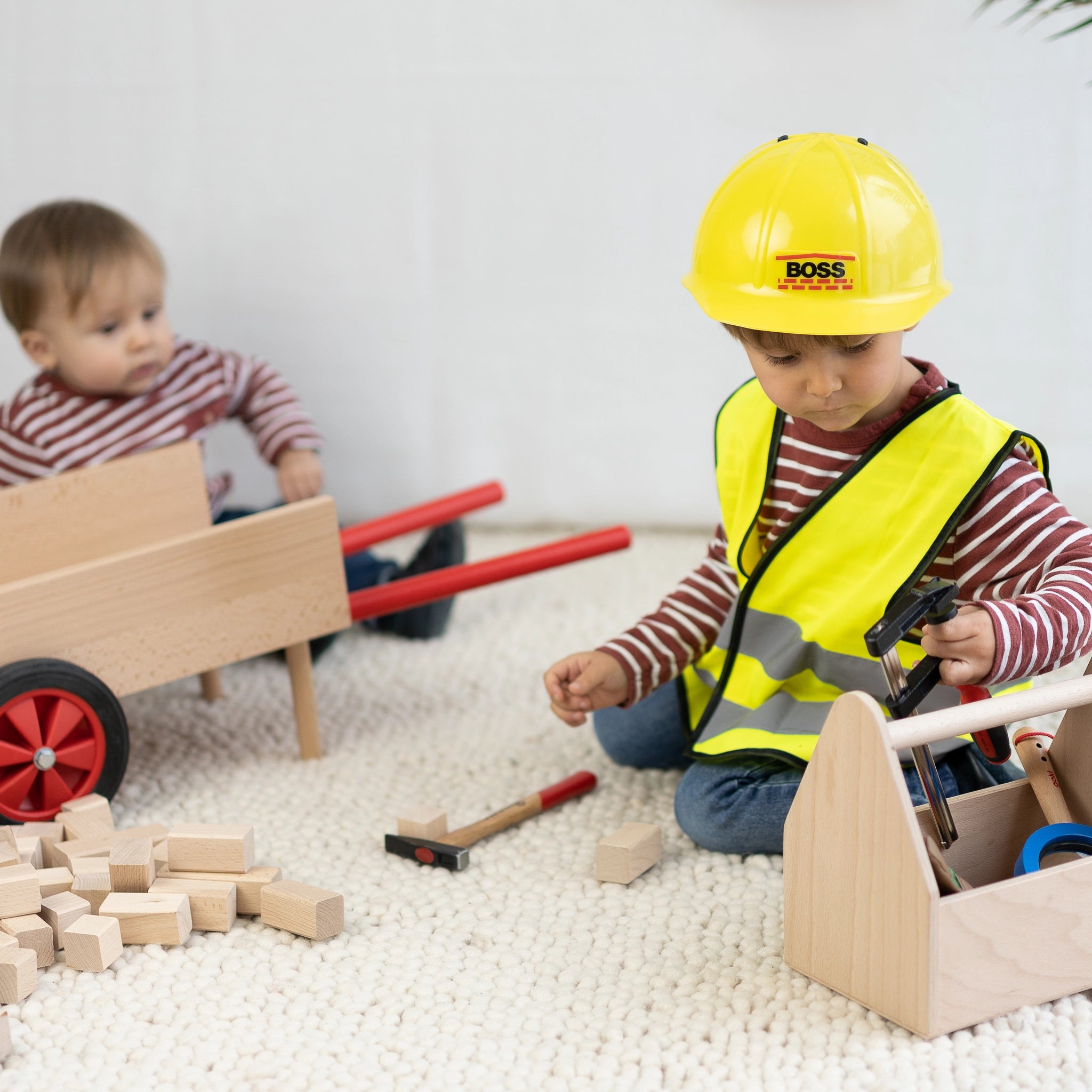 Zwei Kinder spielen mit der Schubkarre aus massivem Buchenholz, ausgestattet mit hochwertigen Gummirädern. Ideal für kleine Handwerker, hergestellt in Vorarlberg, Österreich, von waelderspielzeug.