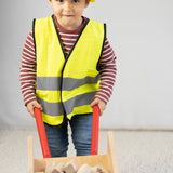 Ein Kind mit gelber Weste und Helm hält eine Schubkarre aus massivem Buchenholz, ideal für kleine Handwerker. Teil der nachhaltigen Eigenmarke waelderspielzeug, hergestellt in Vorarlberg, Österreich.