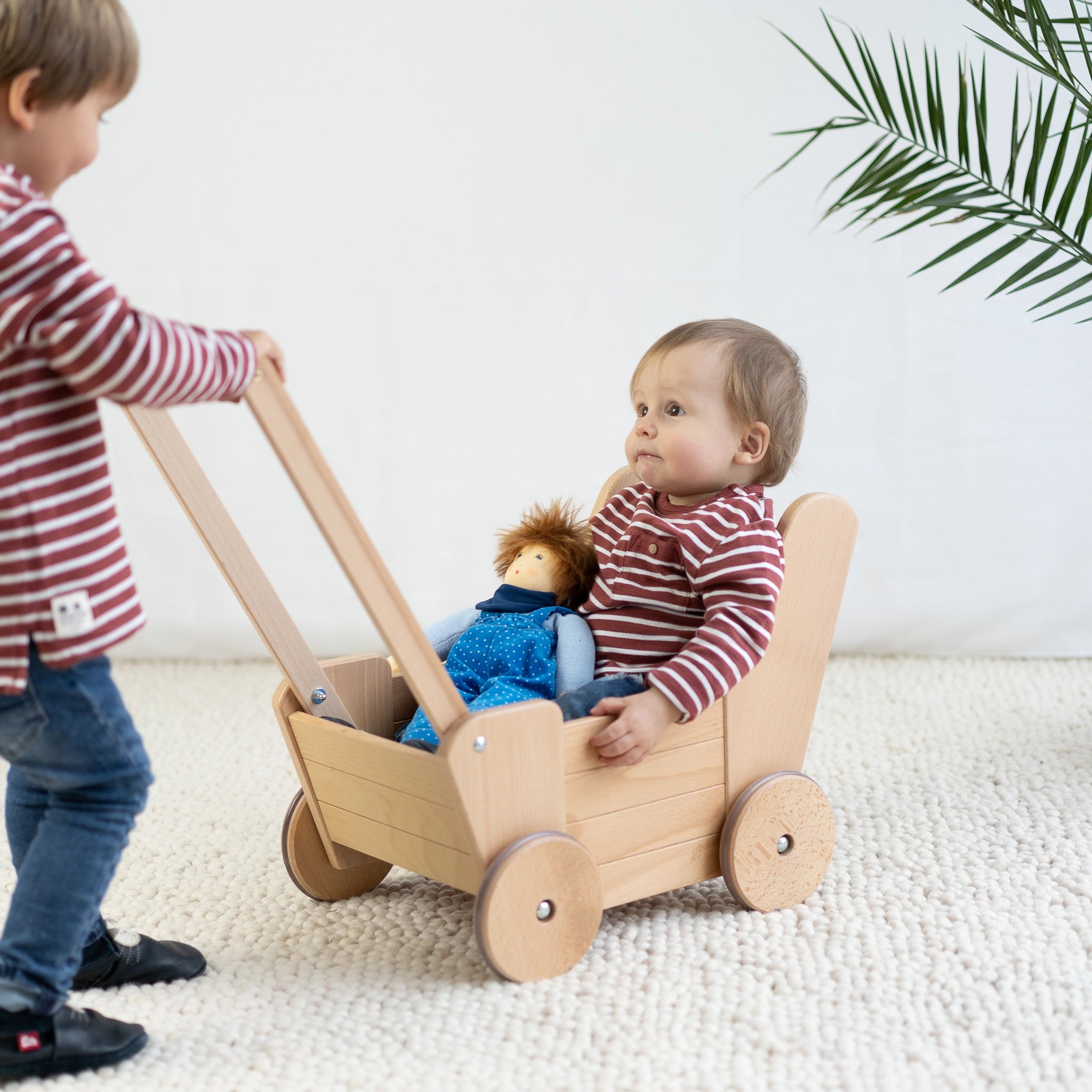 Junge schiebt Puppenwagen aus massivem Buchenholz mit hochwertiger Verarbeitung, inklusive Bettzeug. Nachhaltig in Vorarlberg, Österreich, hergestellt. Ideal für moderne, umweltbewusste Familien.