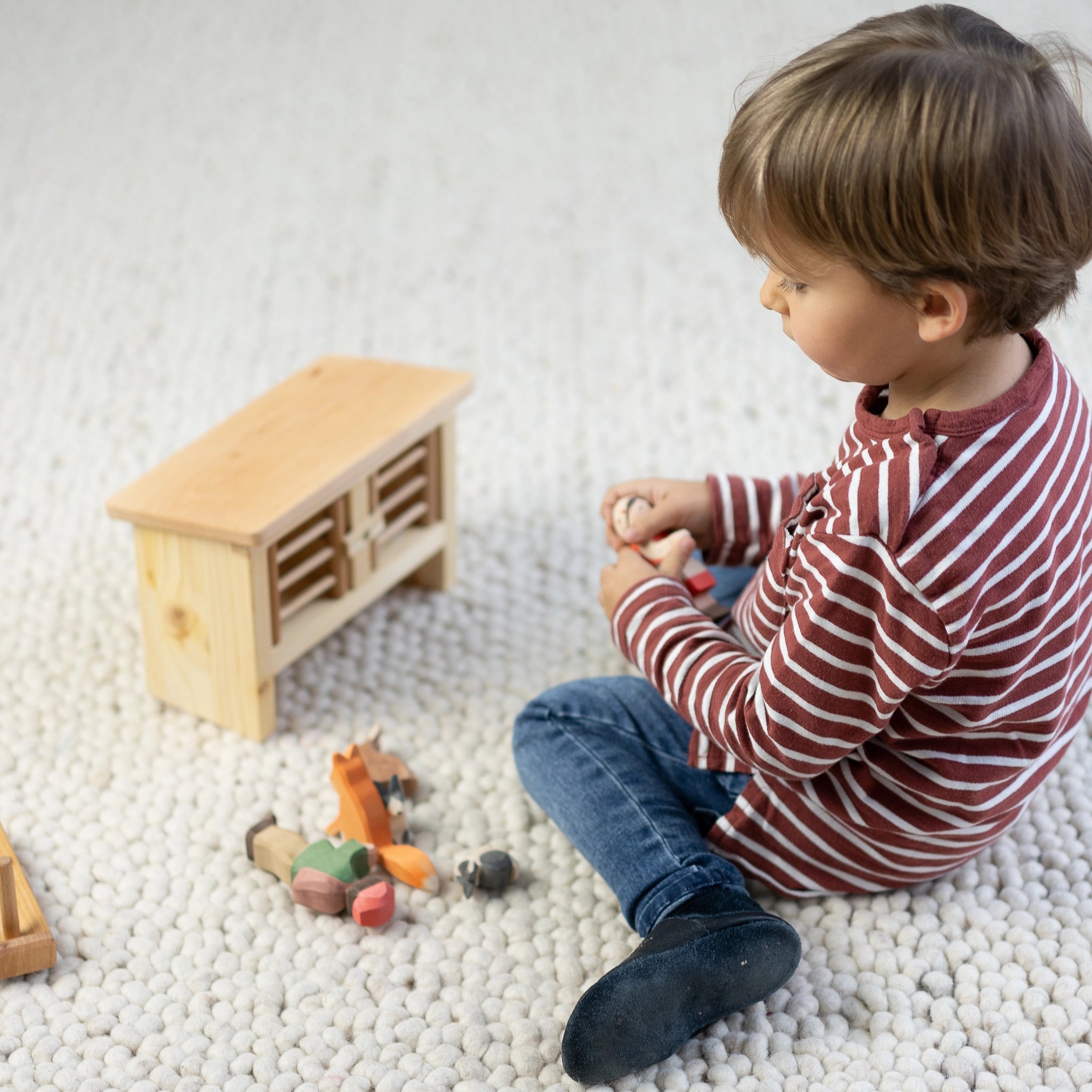 Kind spielt mit einem Hasenstall aus massivem Fichtenholz, veredelt mit Leinöl, mit zwei Boxen zum Öffnen. Perfekt passend für kleine Holzhasen, hergestellt in einer deutschen Holzmanufaktur.