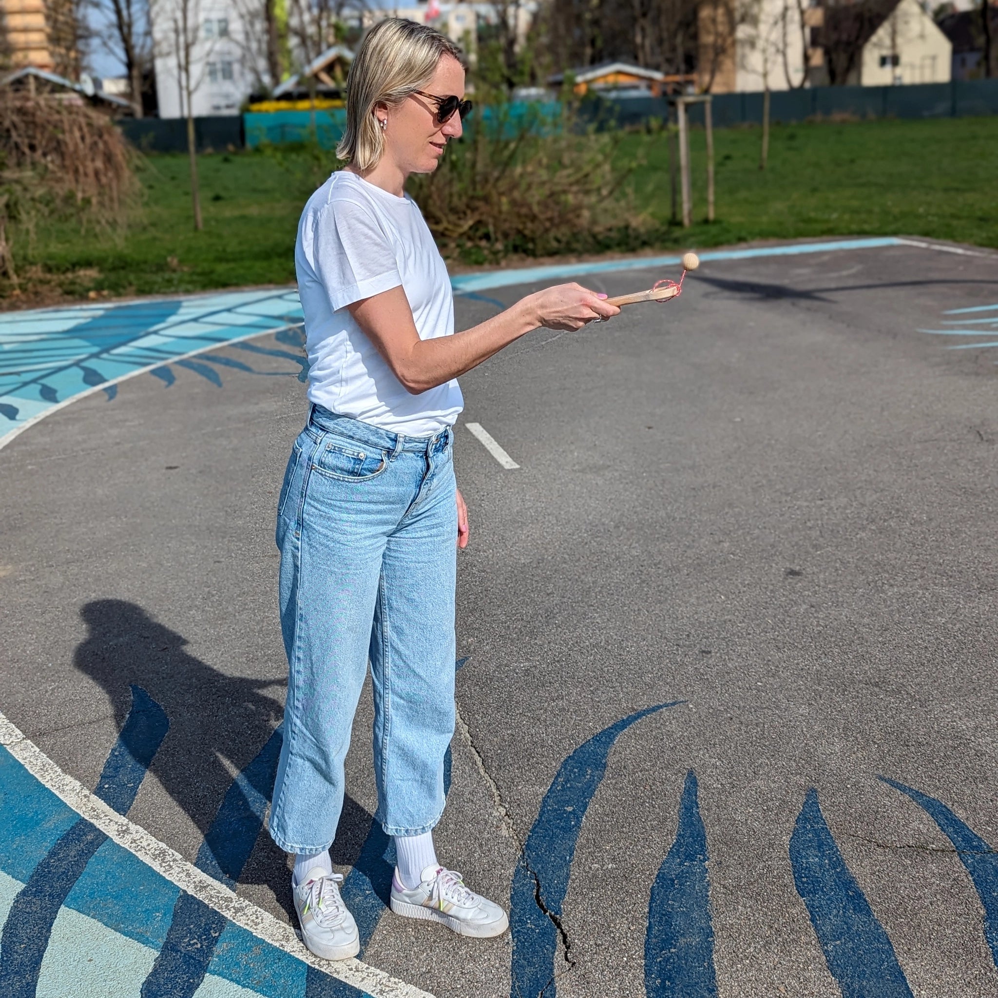 Geschicklichkeitsspiel: Kugelfangspiel aus unbehandeltem Buchenholz, gehalten von einer Frau in einem Parkplatz. Fördert Geschicklichkeit und Koordination, geeignet für Kinder und Erwachsene. Hergestellt in Vorarlberg, Österreich.