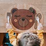 Kinder Tischset: Enjoying Bear, ein Montessori-inspiriertes, wasserabweisendes Korkleder-Design mit liebevollem Bärmotiv, perfekt für den Familientisch. Ein Kind hält ein Set aus Löffel und Gabel.