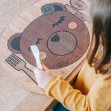 Kinder Tischset: Enjoying Bear aus Korkleder, inspiriert von Montessori, gehalten von einem Mädchen am Tisch. Hergestellt in Österreich, ideal für den Familientisch und fördert nachhaltiges Design.