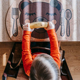 Kind sitzt am Tisch und hält ein Kinder Tischset: Enjoying Bear aus Korkleder. Montessori-inspiriertes Design perfekt für den Familientisch, hergestellt in Österreichs Bregenzerwald.