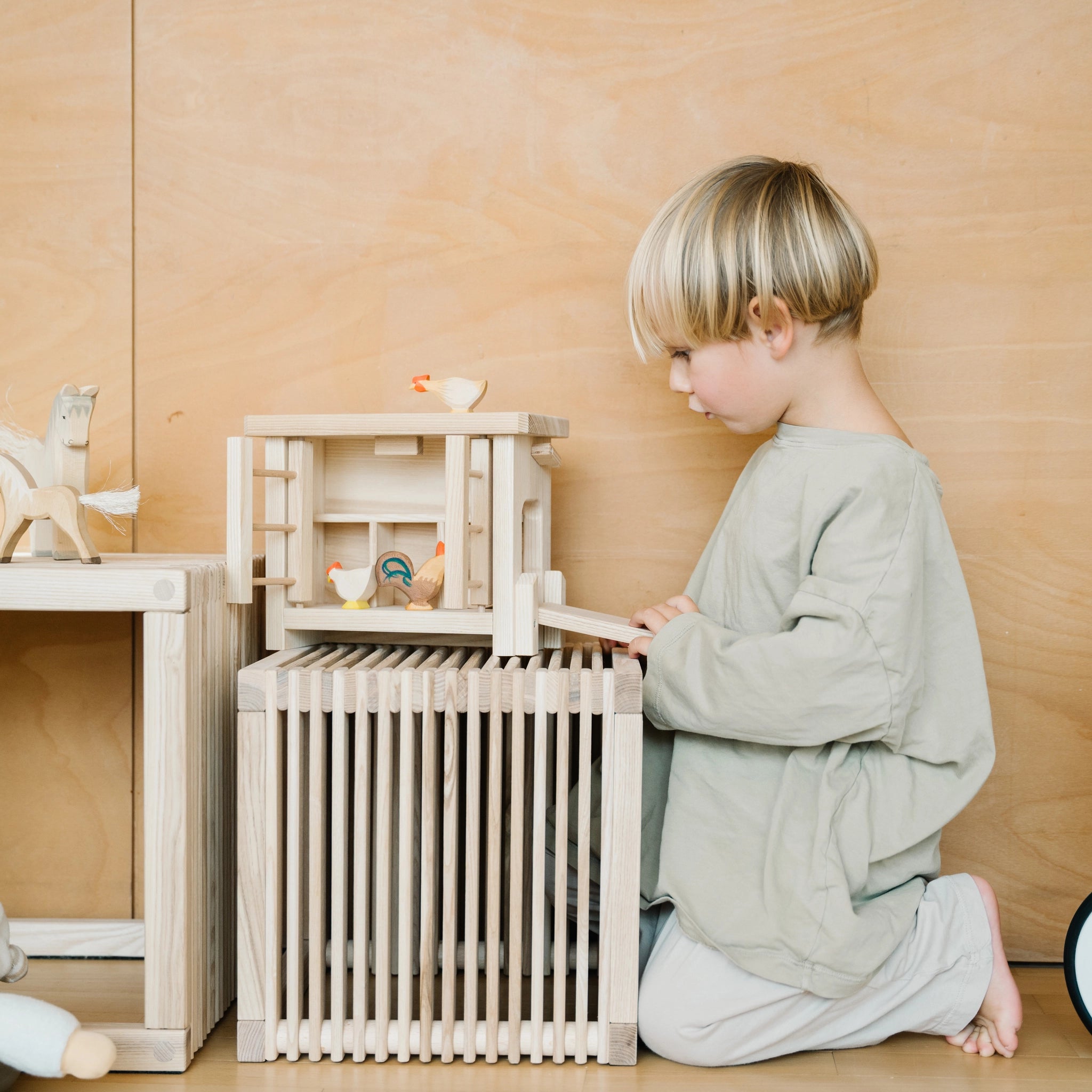 Ein Junge spielt mit einem Kleiner Kinderhocker aus massivem Eschenholz, der als Kinderhocker oder Beistelltisch dient; Teil der nachhaltigen waelderspielzeug Kollektion von KLICKKLACK, aus Vorarlberg, Österreich.