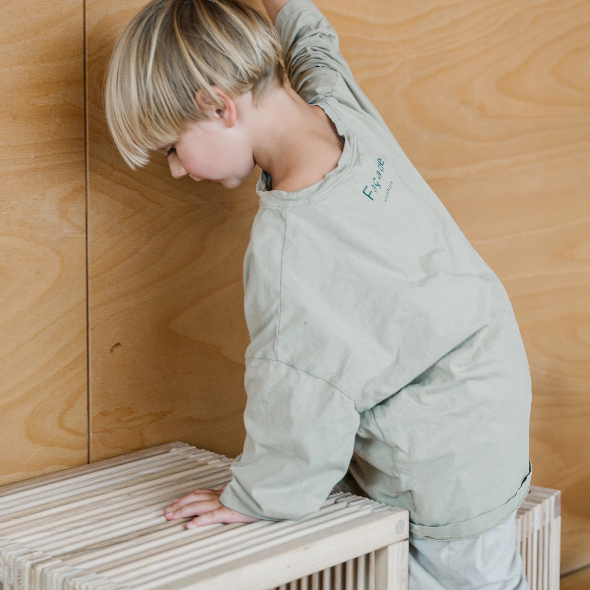 Ein Kind klettert auf ein Regal mit dem Kleiner Kinderhocker aus unbehandeltem Eschenholz, geeignet als Kinderhocker oder Beistelltisch. Hergestellt in Vorarlberg, Österreich, von waelderspielzeug.