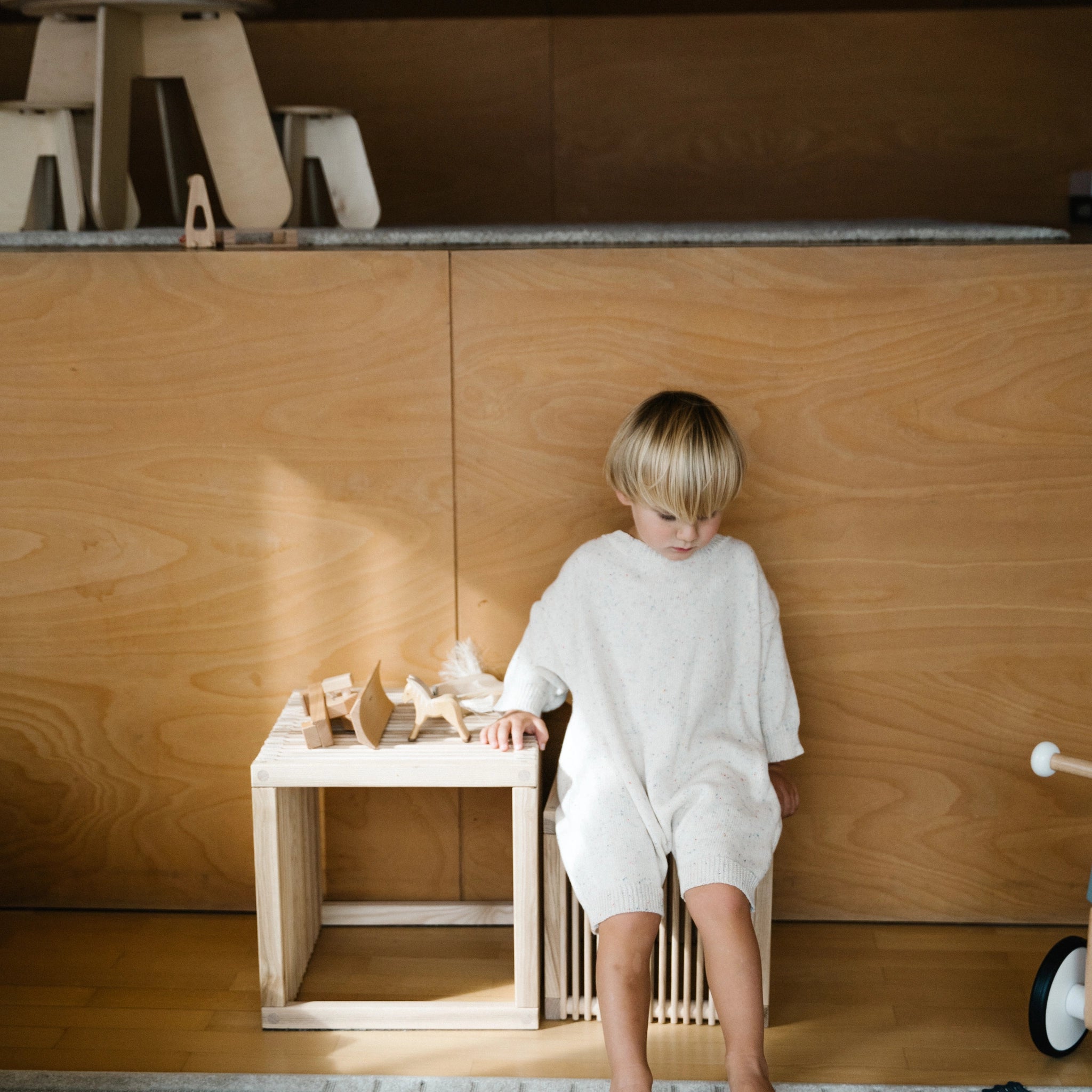 Kleiner Kinderhocker aus massivem, unbehandeltem Eschenholz, auf dem ein Kind sitzt. Vielseitig einsetzbar als Hocker oder Beistelltisch, hergestellt in Vorarlberg, Österreich.