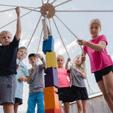 Teamspiel: Kinder-Fröbelturm bunt – Kinder spielen mit farbenfrohen Holzblöcken im Freien, ideal für 4 bis 24 Spieler, Alter 4 bis 7 Jahre, aus nachhaltigem Buchenholz in Vorarlberg hergestellt.