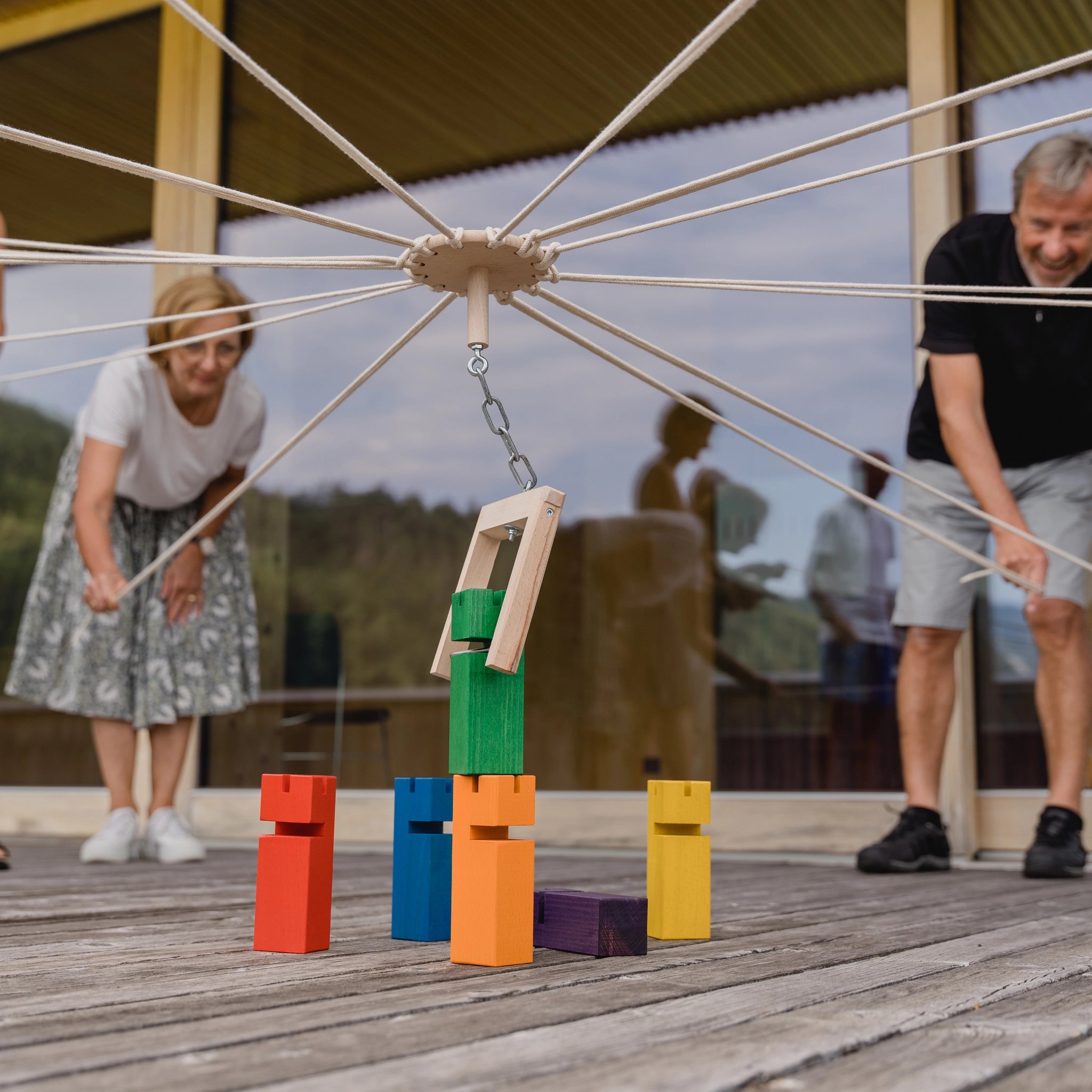 Teamspiel: Fröbelturm bunt, ein robustes Holzspiel für 4 bis 24 Spieler, dargestellt in einem Outdoor-Setting mit spielenden Personen und bunten Blöcken, perfekt für geselliges Spielen und nachhaltige Freude.