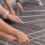 Hände halten ein Seil, während eine Armbanduhr am Handgelenk sichtbar ist, passend zum Teamspiel: Fröbelturm bunt, einem robusten Holzspiel für mehrere Spieler von waelderspielzeug, hergestellt in Österreich.