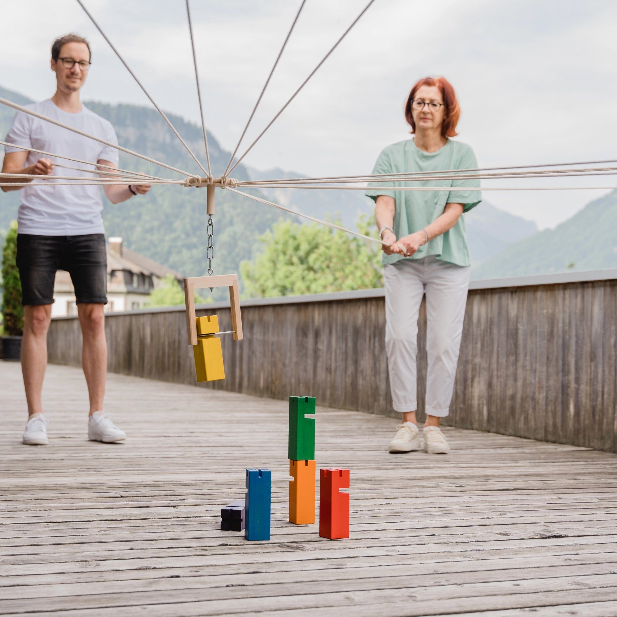 Teamspiel: Fröbelturm bunt, ein Spiel aus massivem Buchenholz, zeigt zwei Personen beim Stapeln bunter Blöcke, ideal für 4 bis 24 Spieler. Nachhaltig in Vorarlberg, Österreich produziert.