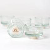 Steckfigur: Teelichthalter Glas, ein Set aus kleinen, klaren Glasschalen auf runden Buchenholzfüßen, eine zeigt das GRIMM'S Logo. Hergestellt in Deutschland, ideal für Snacks oder dekoratives Servieren.