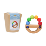 Das Bild zeigt Grimm’s Regenbogen Schiff, ein halbmondförmiges Holzspielzeug mit sechs Regenbogen-Holzkugeln. Links die schlichte Verpackung, rechts das Spielzeug, hergestellt aus massivem, farbig lasiertem Ahorn- und Buchenholz.