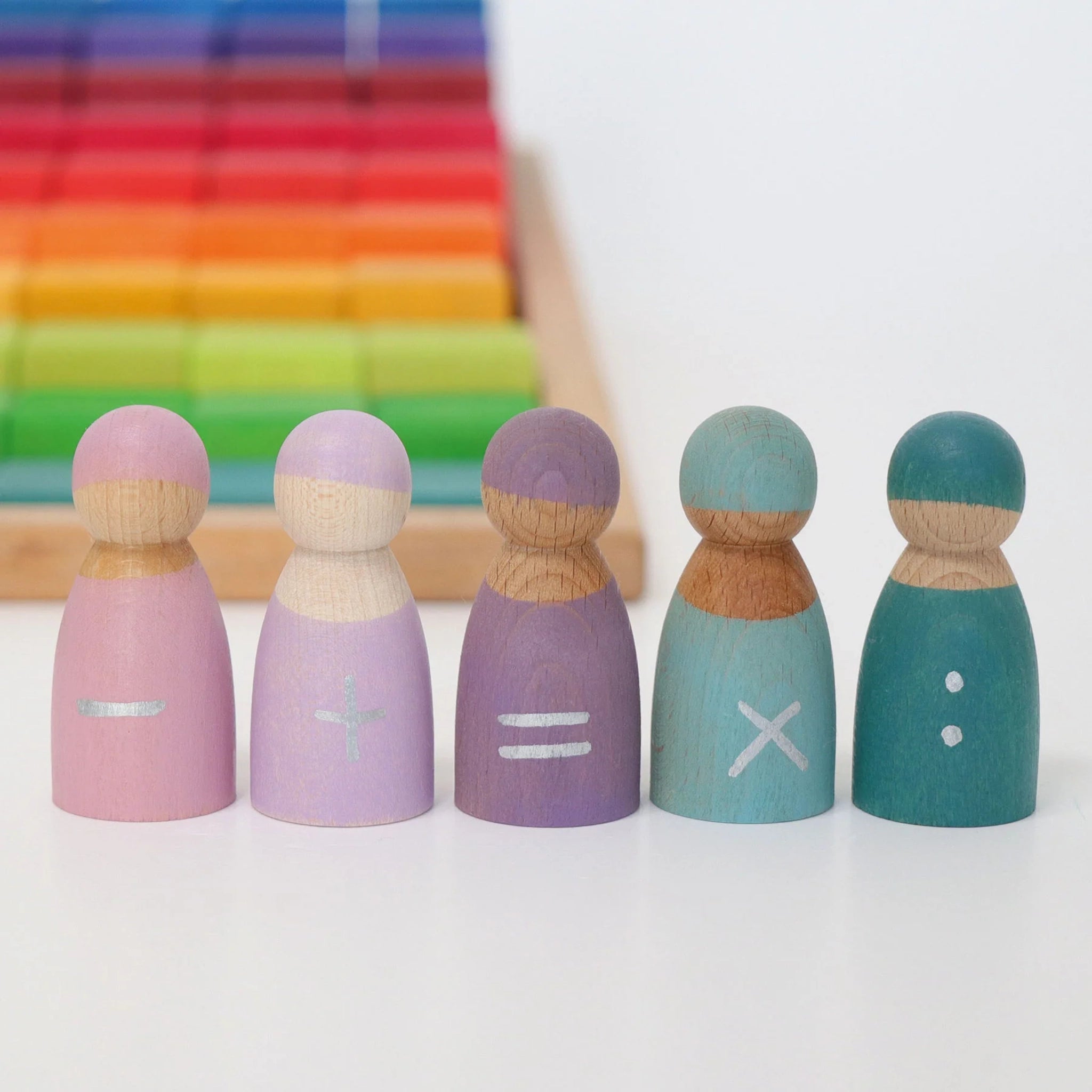 Freies Spiel: Fünf Rechenfreunde – Fünf handbemalte, pastellfarbene Holzfiguren mit Rechenzeichen, aufgereiht vor einem Holztablett mit farbenfrohen Blöcken, bieten einen spielerischen Zugang zu ersten Rechenaufgaben.