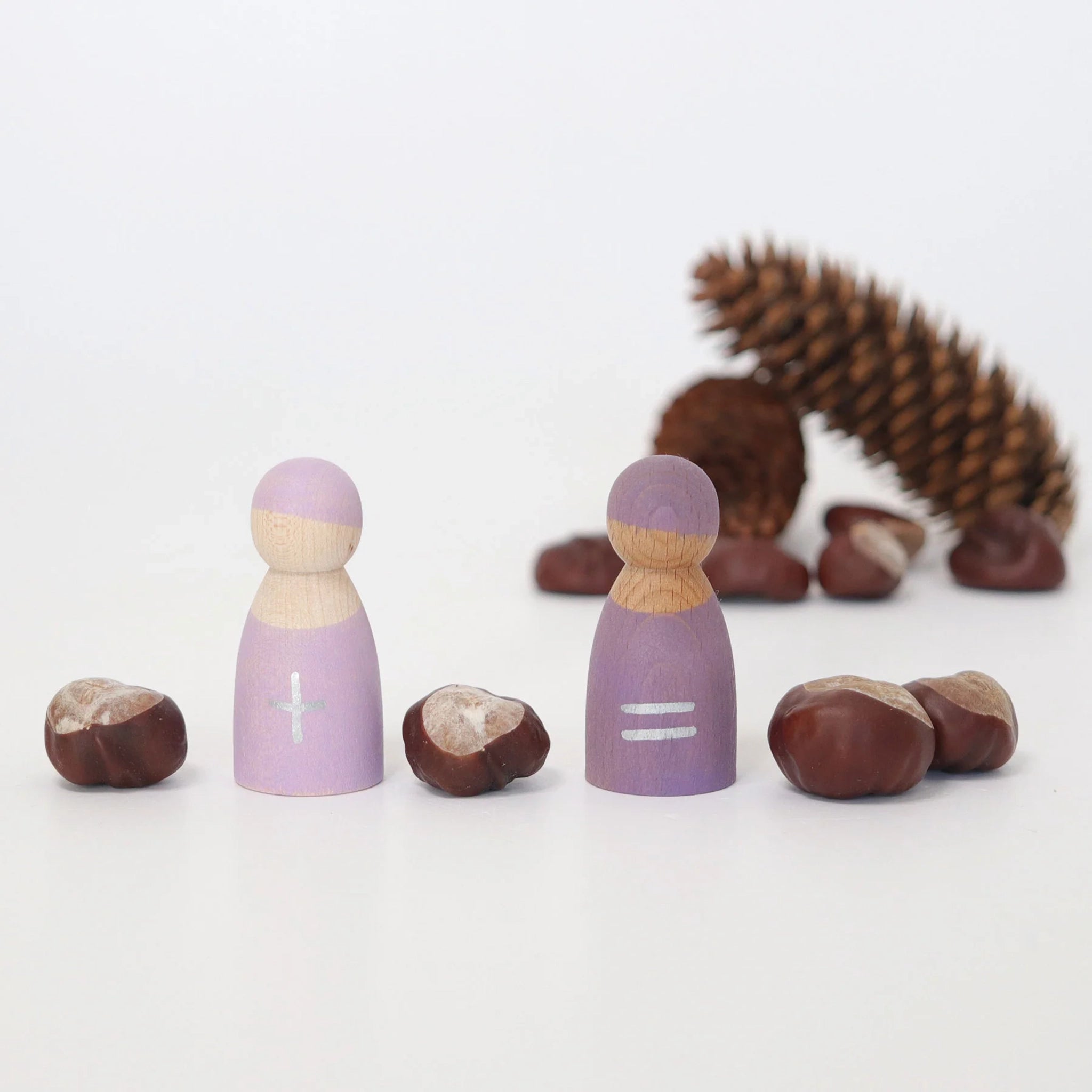 Freies Spiel: Fünf Rechenfreunde aus Holz zeigen plus und gleich Zeichen, flankiert von Kastanien als Zählobjekte. Ein spielerischer Lernansatz für erste Rechenaufgaben durch haptisches Erleben.