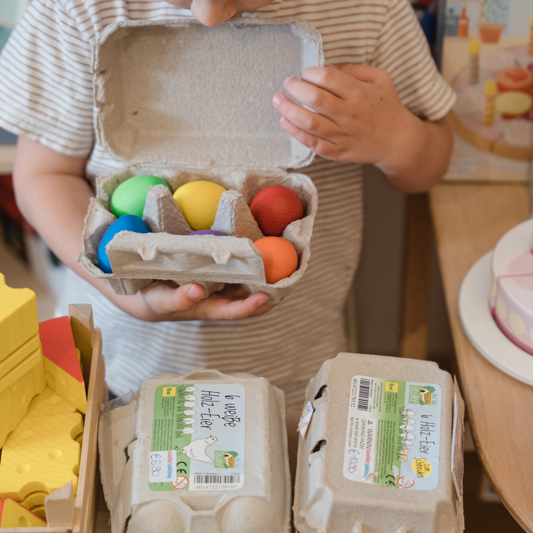 Lebensmittel: Eier weiß im Karton, gehalten von einem Kind. Sechs weiße Eier, ideal für Kinderküchen oder Kaufmannsläden, hergestellt aus Buchenholz in einer deutschen Manufaktur.