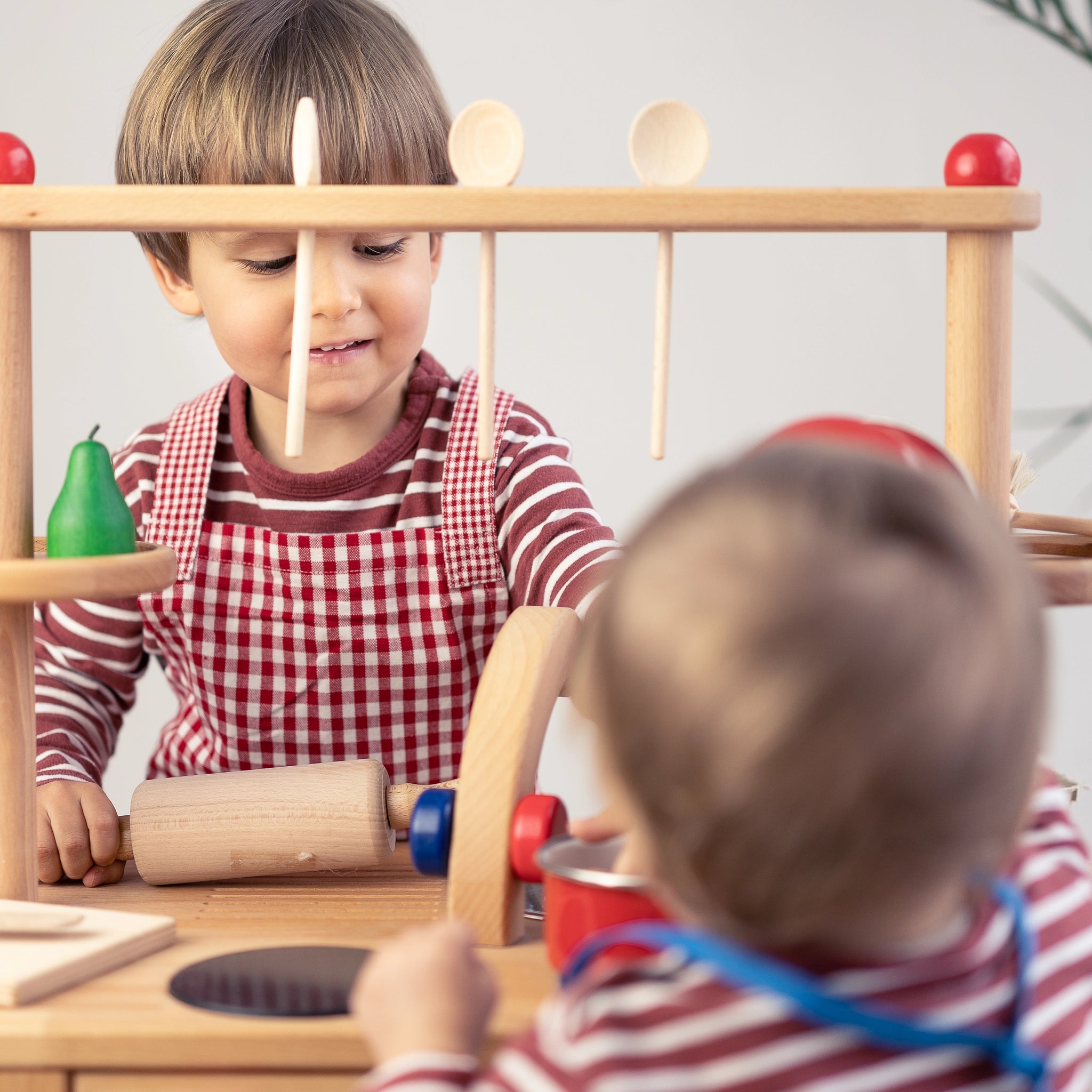 Kindernudelholz aus unbehandeltem Buchenholz, robust und ideal für kleine Köche. Zwei Kinder spielen damit, inspiriert von nachhaltigem Design und Ästhetik, passend zur modernen Zielgruppe von KLICKKLACK.