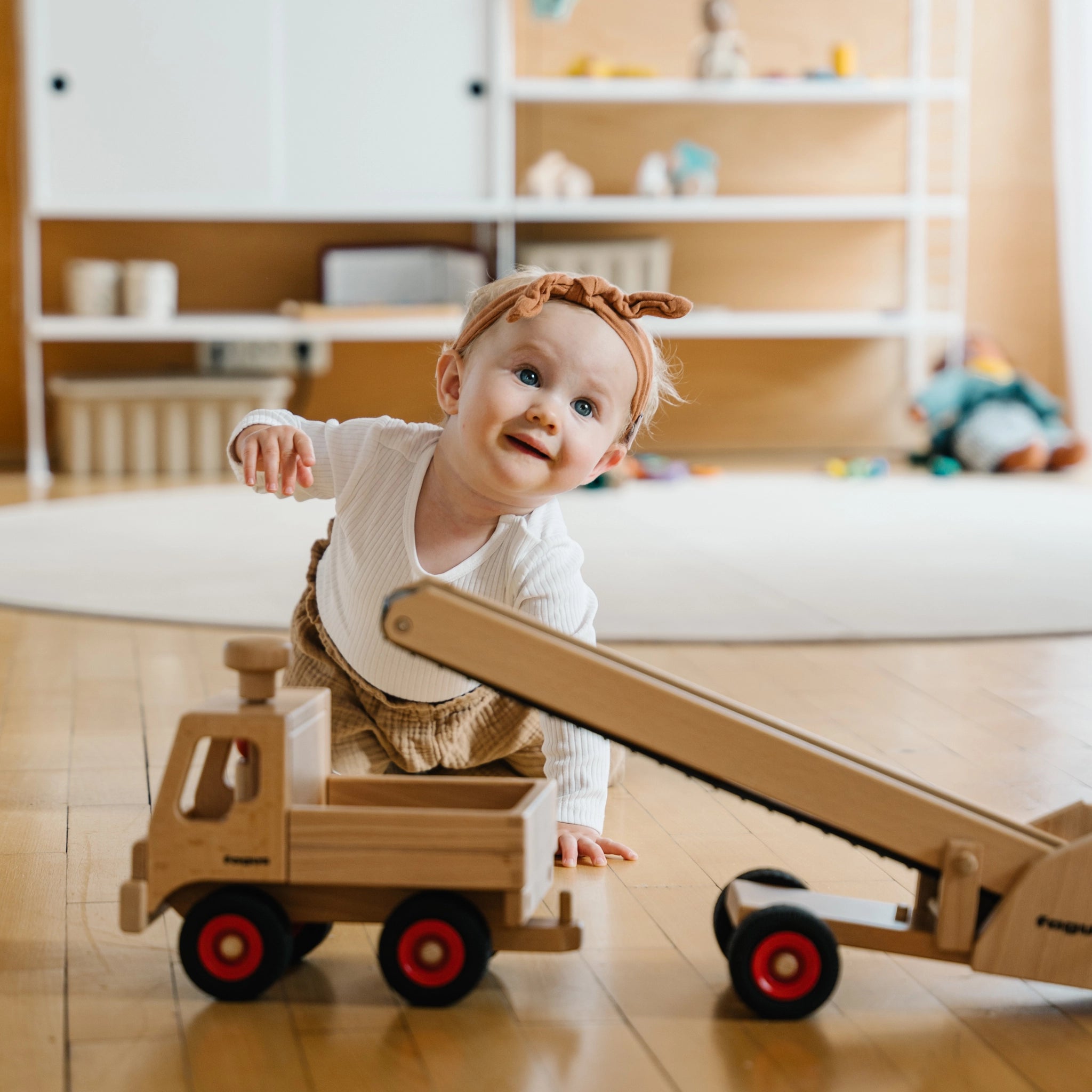 Holzfahrzeug: Unimog aus massivem Buchenholz, spielend von einem Baby genutzt. Lenkbares Design mit robuster Ladefläche, hergestellt in Deutschland, kompatibel mit Fagus-Anhängern.