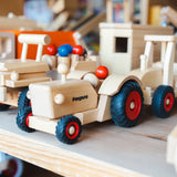 Holzfahrzeug: Traktor aus massivem Buchenholz, präsentiert auf einem Regal. Detailreiche Ansicht der lenkbaren Räder, inklusive zwei Fahrerfiguren, ideal für vielseitigen Spielspaß. 