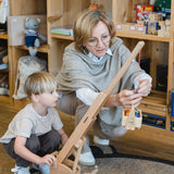 Eine Frau und ein Junge spielen mit dem Holzfahrzeug: Mobilkran, einem drehbaren, höhenverstellbaren Kranarm aus massivem Buchenholz, inklusive Kranführerfiguren.