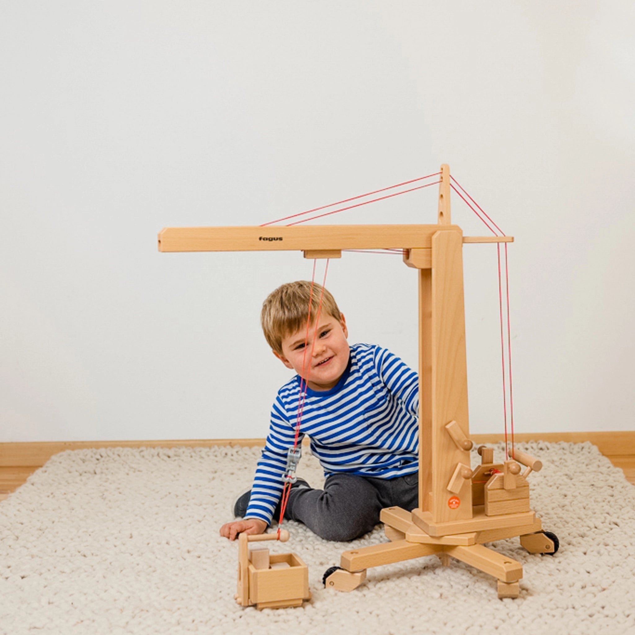 Junge spielt auf dem Boden mit dem Holzfahrzeug: Hochkran aus massivem Buchenholz, drehbarer Turm und höhenverstellbarer Ausleger. Fördert kreatives Spielen und technische Neugier.