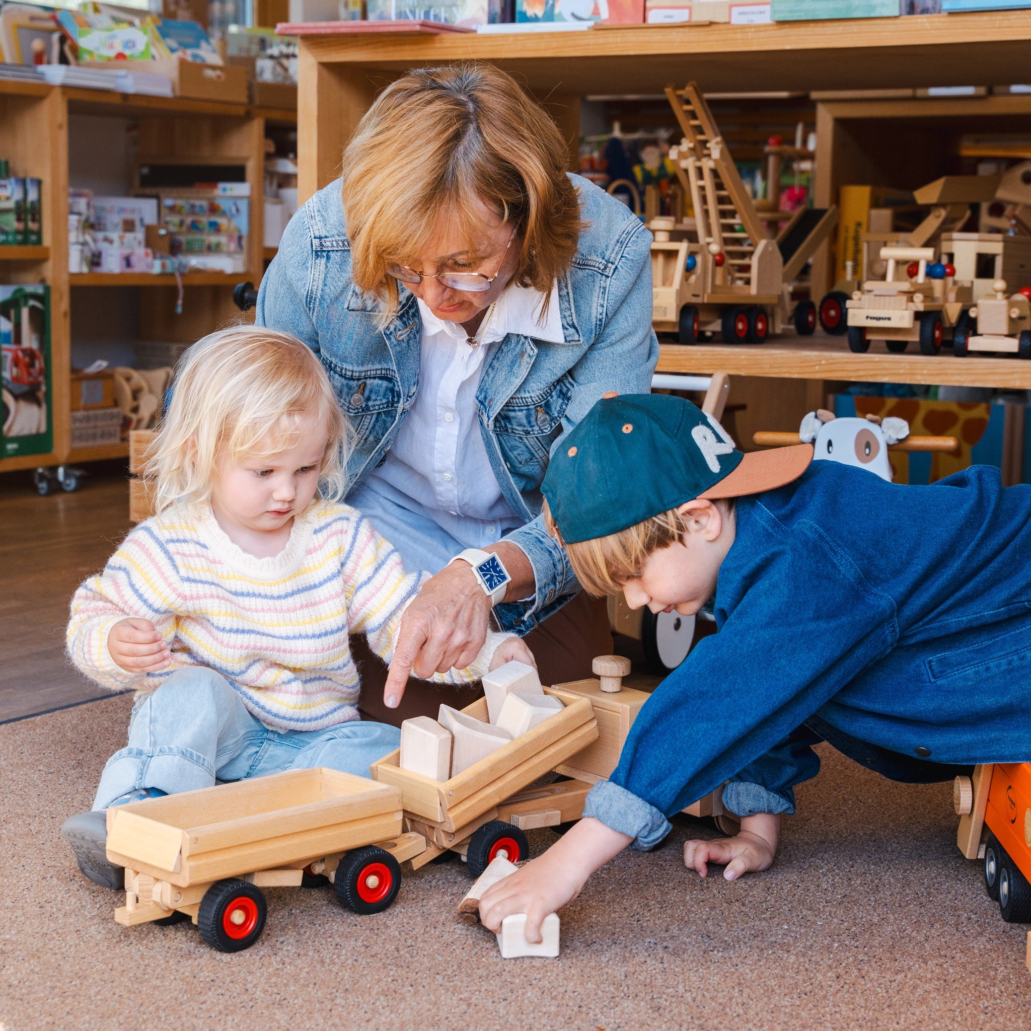 Holzfahrzeug: LKW-Kipper, ein aus massivem Buchenholz gefertigtes Spielzeug mit lenkbarer Funktion, kippbarer Ladefläche und zwei Fahrerfiguren, gezeigt im Spiel mit Kindern.