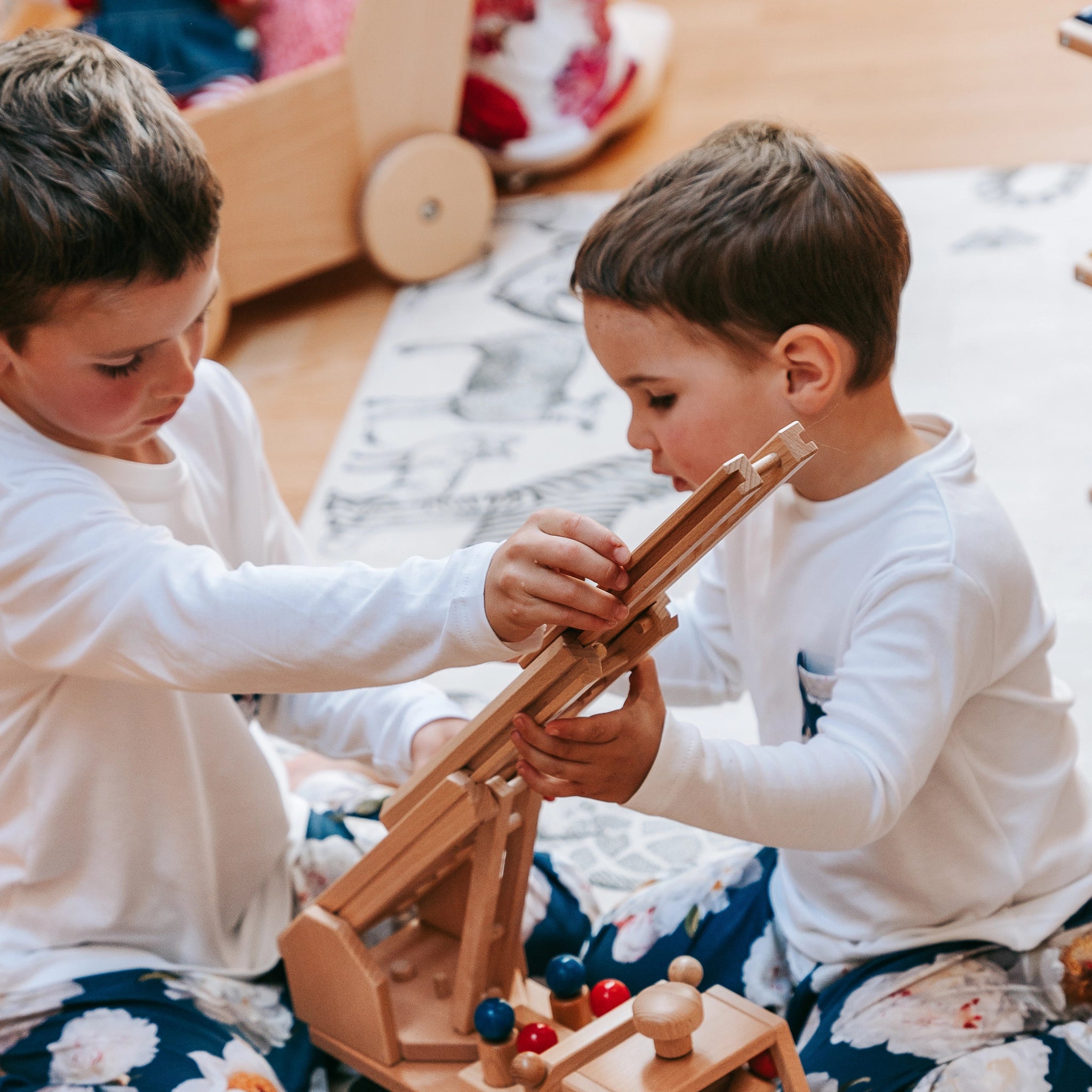 Holzfahrzeug: Feuerwehrauto aus massivem Buchenholz, mit lenkbarem Fahrzeug und drehbarer, höhenverstellbarer Leiter. Zwei Jungen spielen mit dem robusten Spielzeug, das in Deutschland gefertigt wurde.