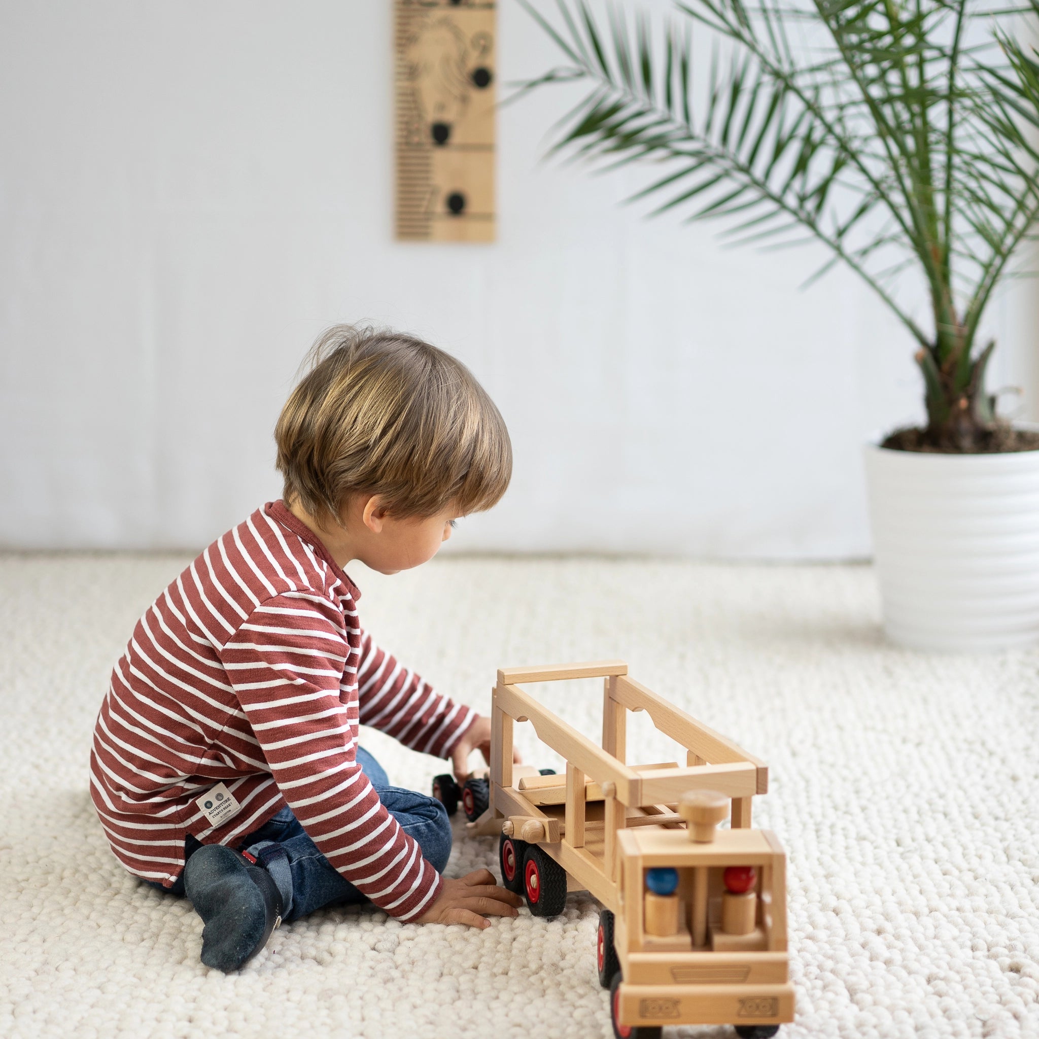 Holzfahrzeug: Autotransporter aus Buchenholz, spielender Junge darauf sitzend. Enthält zwei Püppchen und ein Knubbel-Auto Speedy, gefertigt in Deutschland, ideal für kreative Spiele im Kinderzimmer.