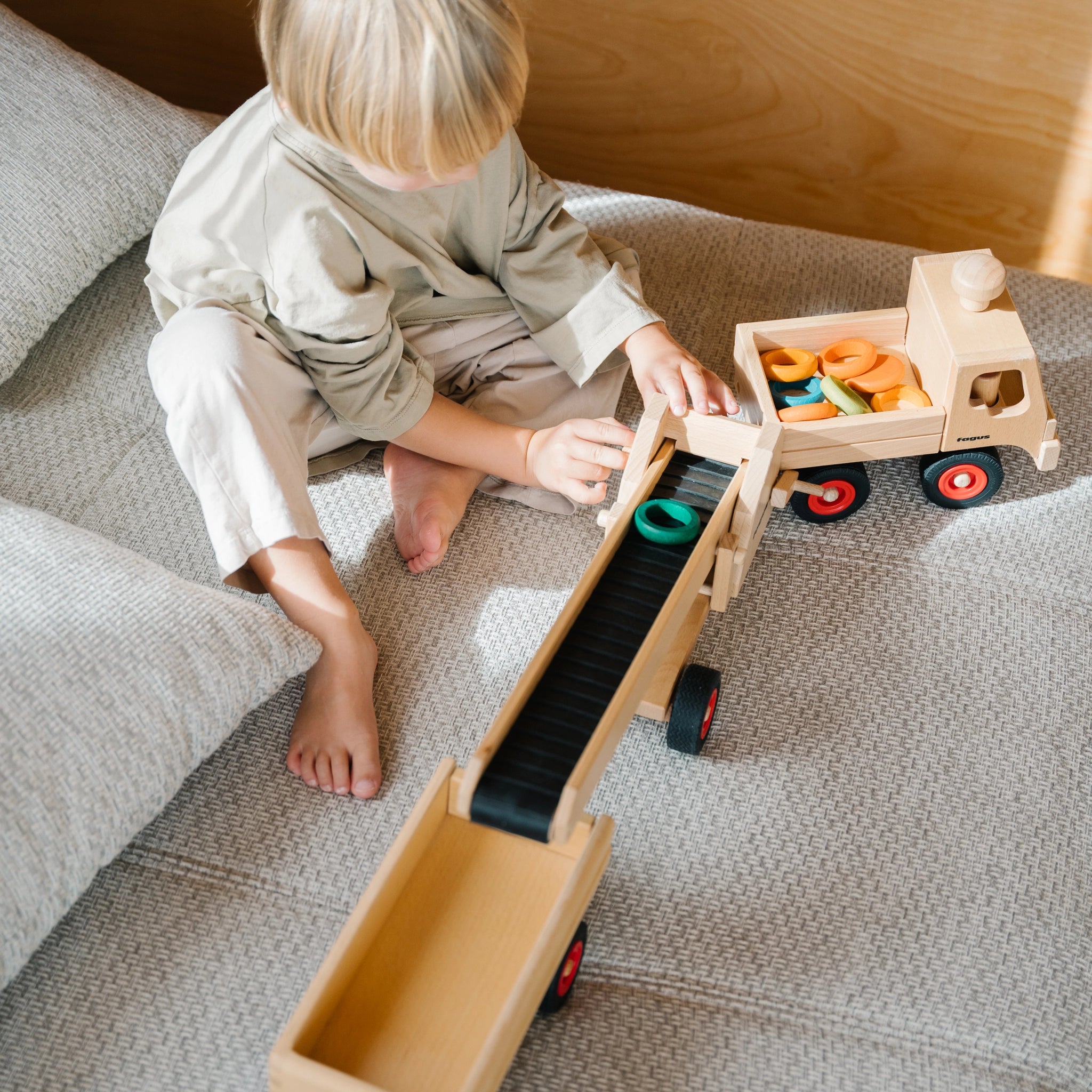 Zubehör: Förderband aus massivem Buchenholz, ideal für Fagus-Fahrzeuge, zeigt ein Kind beim Spielen, symbolisiert Nachhaltigkeit und sozial-faire Produktion, hergestellt in einer deutschen Werkstätte.