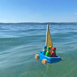 Holzfahrzeug: Strandsegler, ein schwimmfähiges Holzspielzeug-Set mit Segelschiff und vier Matrosen, im Wasser treibend. Ideal für drinnen und draußen, hergestellt aus lasiertem Lindenholz in Deutschland.