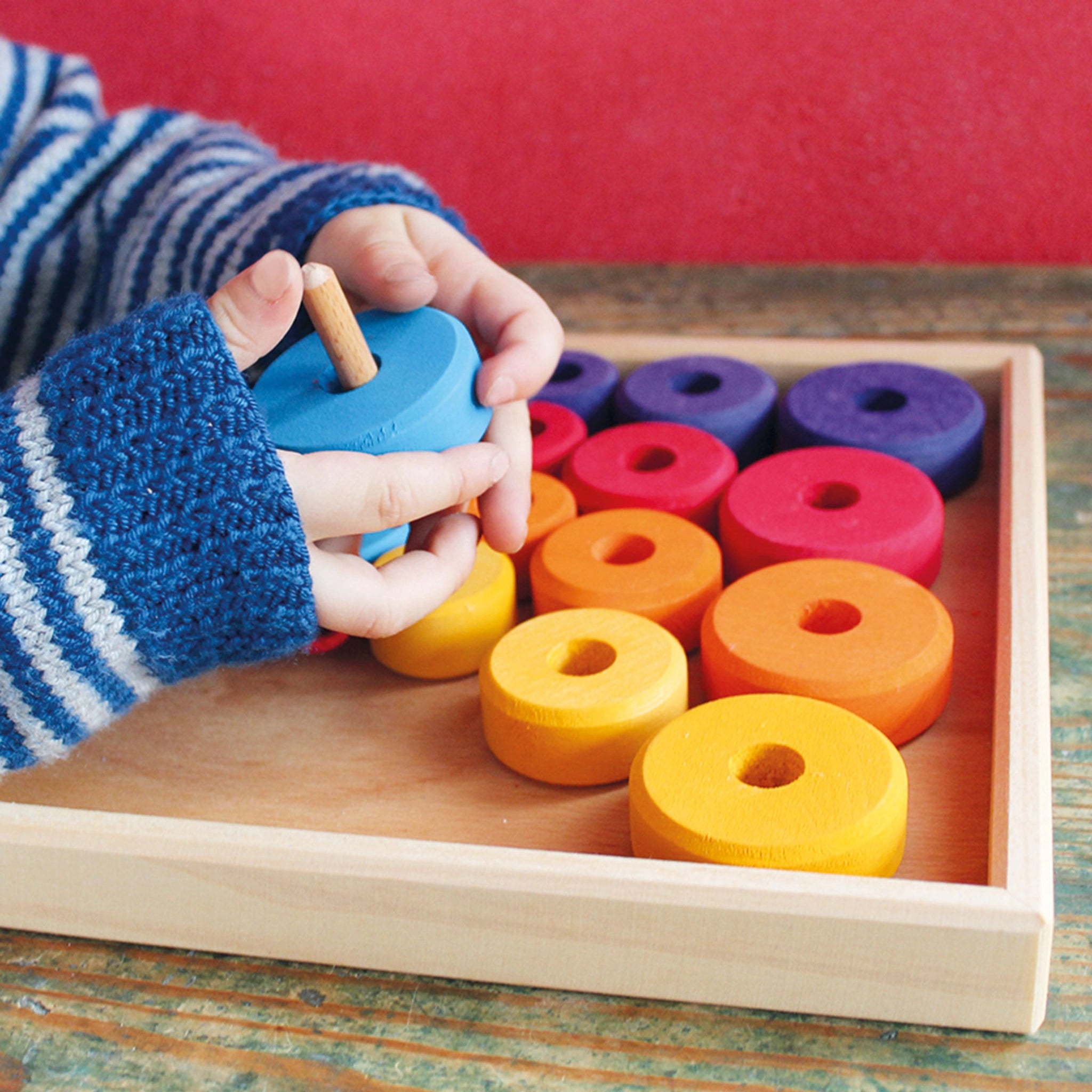 Motorikspiel: Erstes Fädelspiel mit einem Kind, das bunte Holzscheiben auf eine Holznadel auffädelt. Ideal für kleine Hände, hergestellt aus farbig lasiertem Lindenholz in Deutschland.