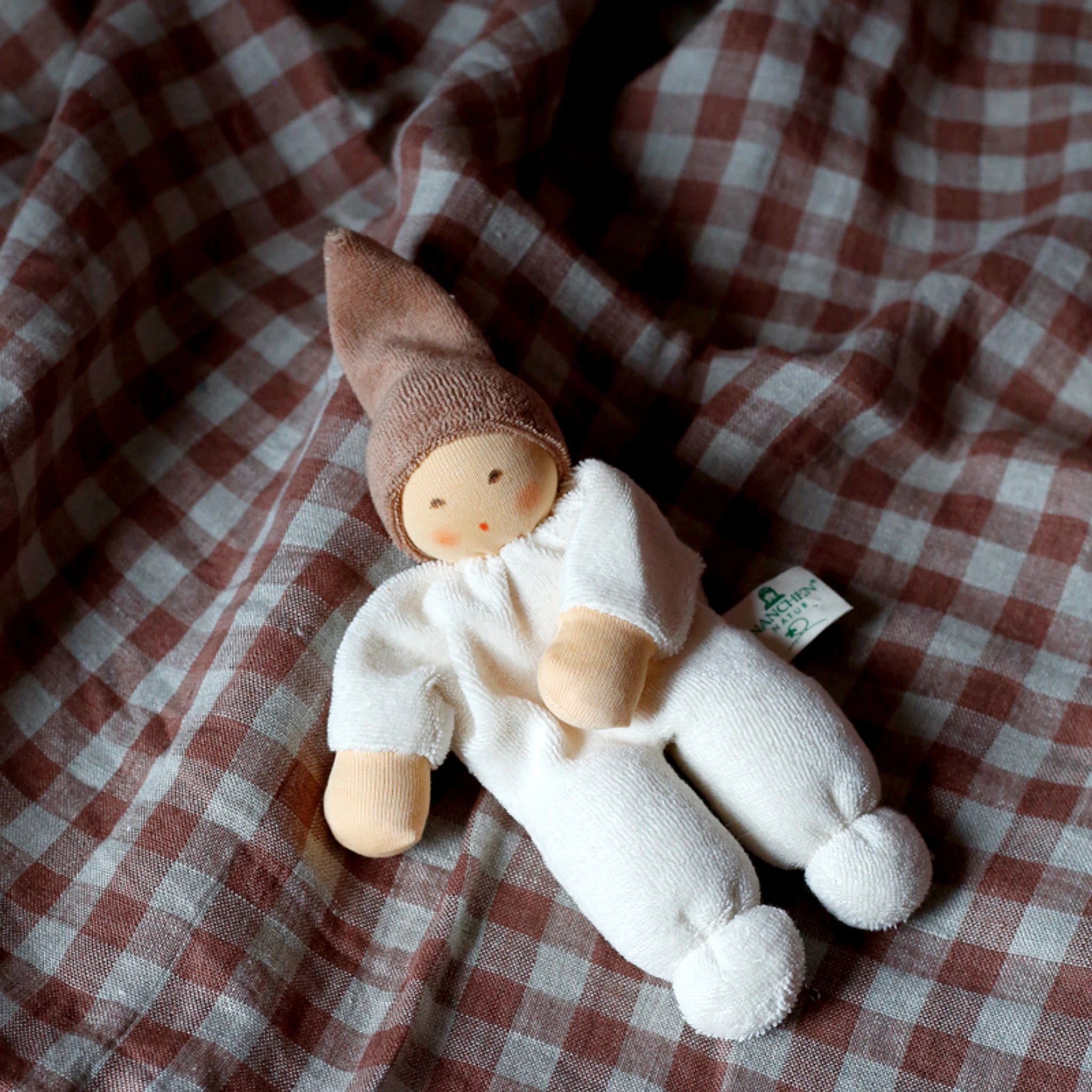 Puppe: Nucki beige auf einer Decke liegend, aus weichem Bio-Baumwollefrottee, ideal zum Greifen und Kuscheln. Sichtbarer Stoff und Label, sanft klingelndes Glöckchen im Inneren, handgefertigt in Deutschland.