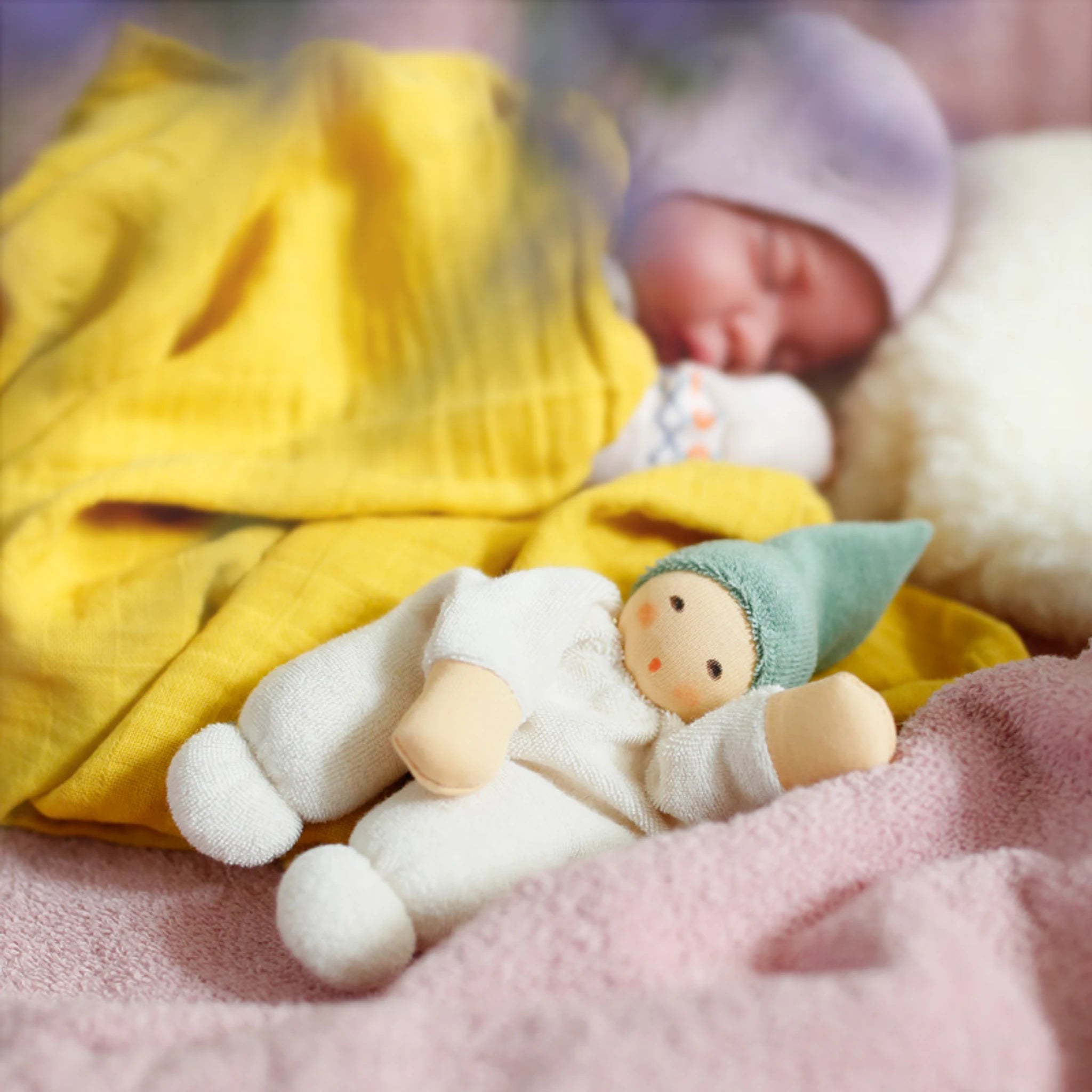 Puppe: Nucki salbei, ein Babyspielzeug aus weichem Bio-Baumwollefrottee, liegt neben einem schlafenden Baby auf einer Decke. Ideal zum ersten Greifen und Kuscheln.