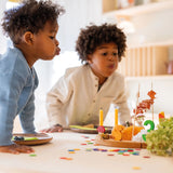 Zwei Kinder blasen Kerzen auf einem herbstlich dekorierten Tablett aus. Freies Spiel: Konfettitaler Regenbogen aus Sperrholz verstreut auf dem Tisch, ideal für festliche Dekorationen. Nachhaltig hergestellt in Deutschland.