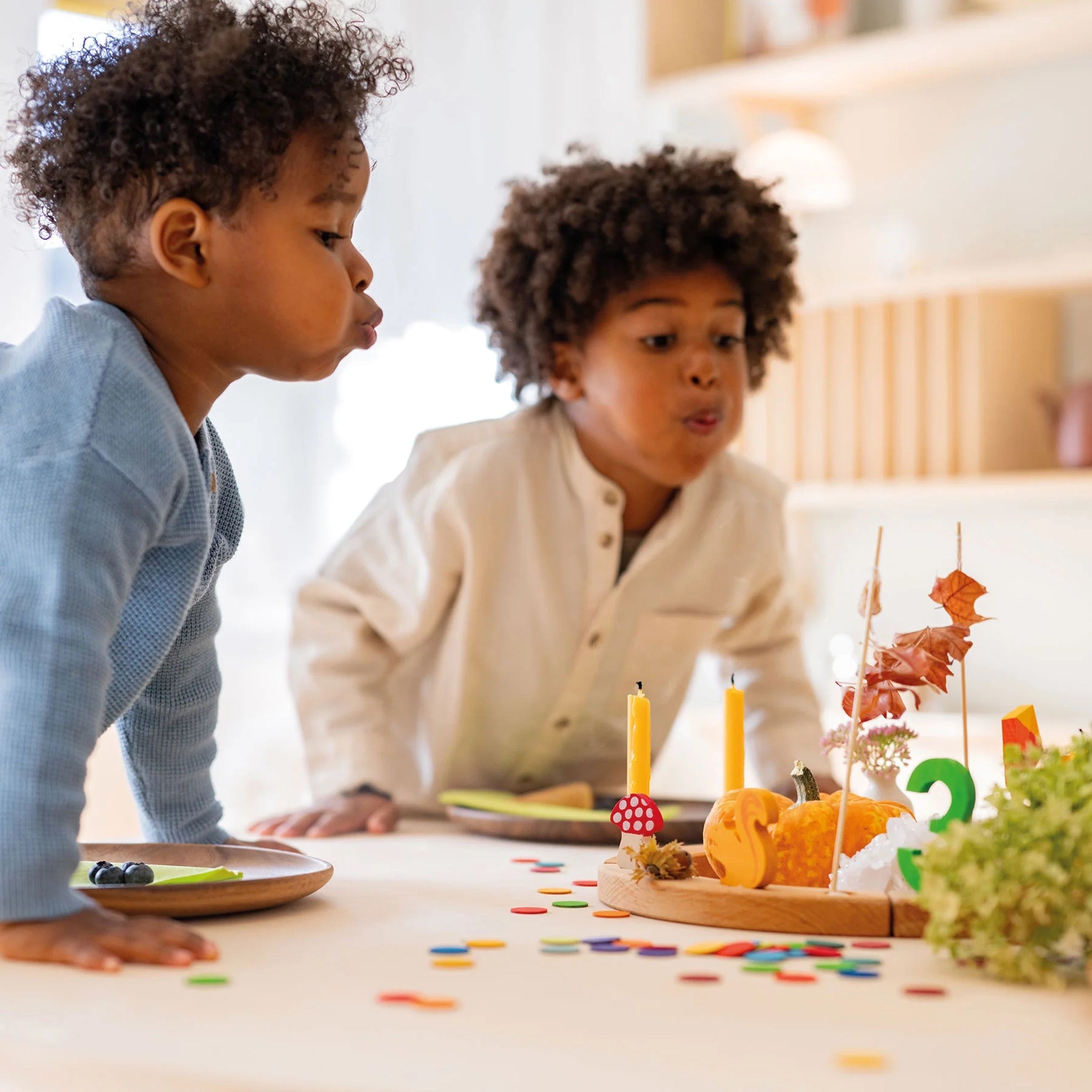 Zwei Kinder blasen Kerzen auf einem herbstlich dekorierten Tablett aus. Freies Spiel: Konfettitaler Regenbogen aus Sperrholz verstreut auf dem Tisch, ideal für festliche Dekorationen. Nachhaltig hergestellt in Deutschland.