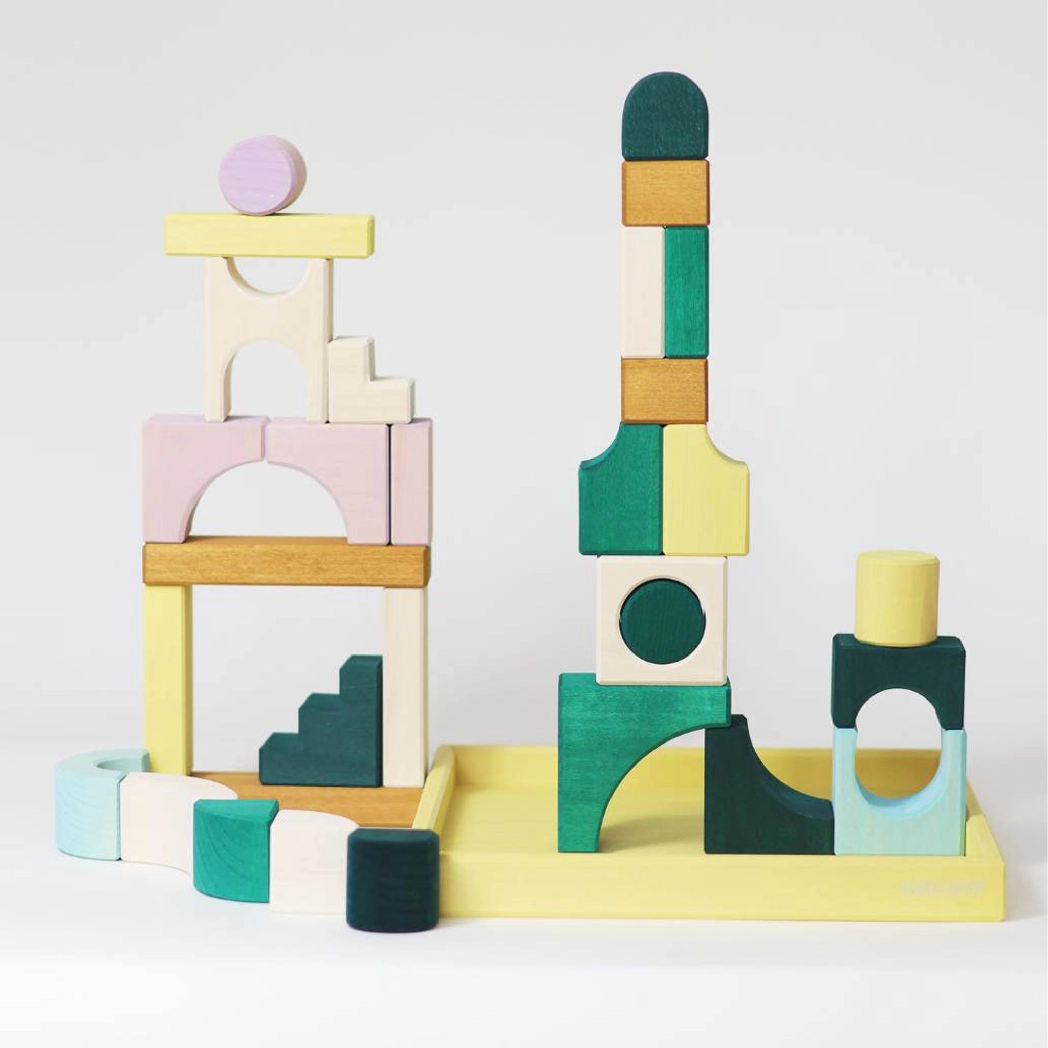 Bauwelt: Movement zeigt pastellfarbene Holzbausteine in Form von Bögen, Halbkreisen, Rechtecken, Zylindern und Treppen. Diese sind kunstvoll zu zwei kleinen Architektur-Türmen auf einem Tablett gestapelt.