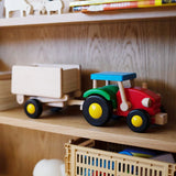 Holzfahrzeug: Traktor mit Anhänger aus Buchen- und Ahornholz, bunt bemalt, steht auf einem Regal. Der Anhänger ist abnehmbar und kippbar, ideal für Kinder. Hergestellt in Polen.