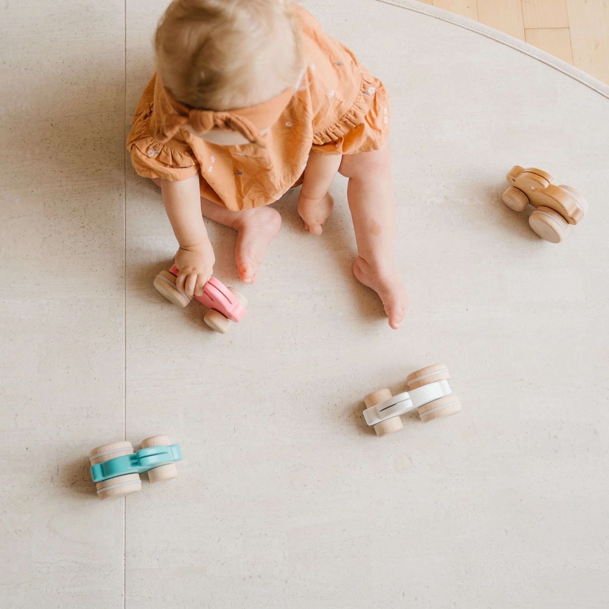 Motorikspiel: Hoppelhase natur – Ein Baby spielt auf dem Boden mit einem Holzspielzeughasen, der beim Anstoßen das Hinterteil bewegt und leise auf Silikonrollen hoppelt.