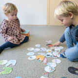 Memory: Chicks & Chickens, Kinder spielen auf dem Boden, umgeben von Papierschnipseln. Das Spiel fördert Gedächtnis und Konzentration mit liebevoll illustrierten Hennen- und Küken-Paaren, ideal für Kinder ab 3 Jahren.