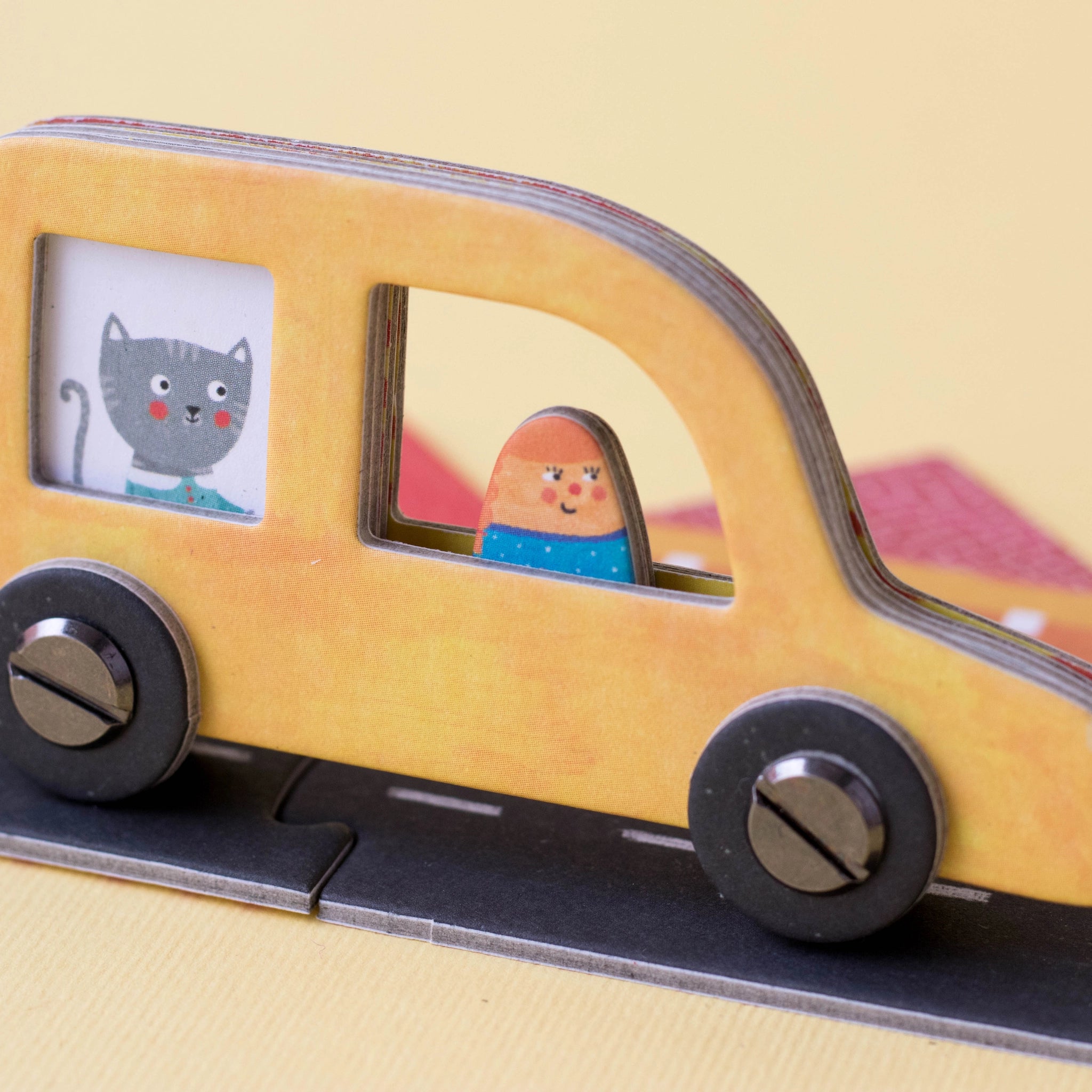 Gesellschaftsspiel: Roads mit einem Spielzeugauto, das einen Cartoon-Charakter im Fenster zeigt. Hergestellt aus recyceltem Karton und FSC-Papier, bietet kreatives Spielvergnügen für Familien oder Solo-Abenteuer.