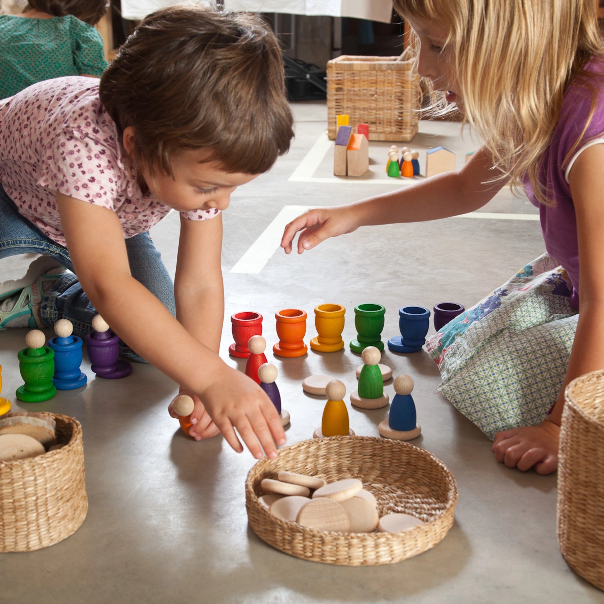 Freies Spiel: Nins, Mates & Coins - Zwei Kinder spielen mit handgefertigten Holzfiguren aus nachhaltiger Forstwirtschaft, inklusive sechs Nins-Figuren, sechs Töpfchen und sechs Plättchen für kreatives Spielen.