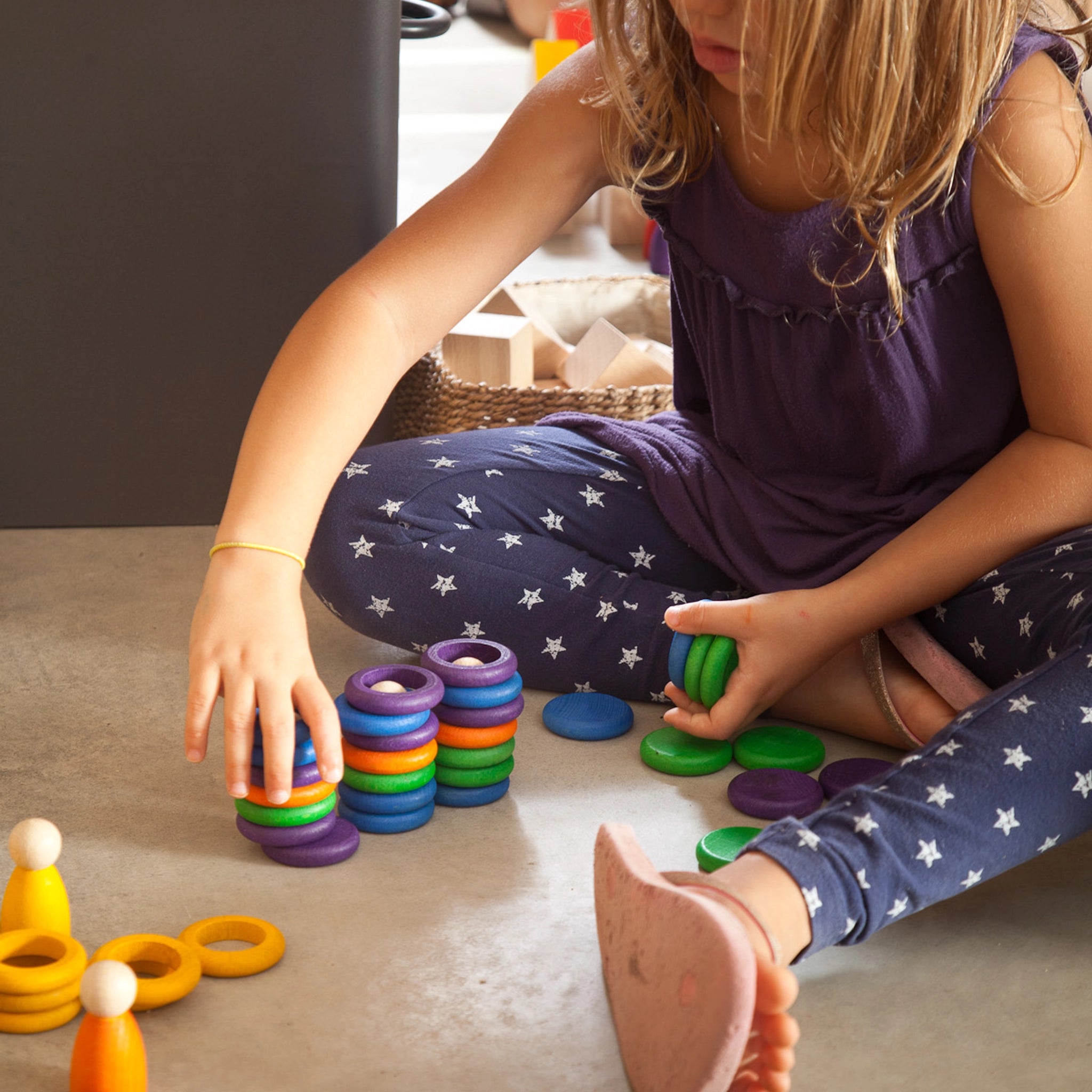 Freies Spiel: Nins, Rings & Coins – Ein Mädchen spielt mit farbenfrohen Holzringen aus nachhaltigem Anbau, ideal für kreatives Spiel. Handgefertigt in Spanien, fördert es kindliche Entwicklung und Fantasie.