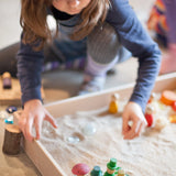 Freies Spiel: Play Box - Mädchen spielt mit Sand, inspiriert vom Montessori-Konzept. Aus nachhaltig geforstetem Holz, handgefertigt in Spanien, ideal für sensorische Erlebnisse und freies Spielen.