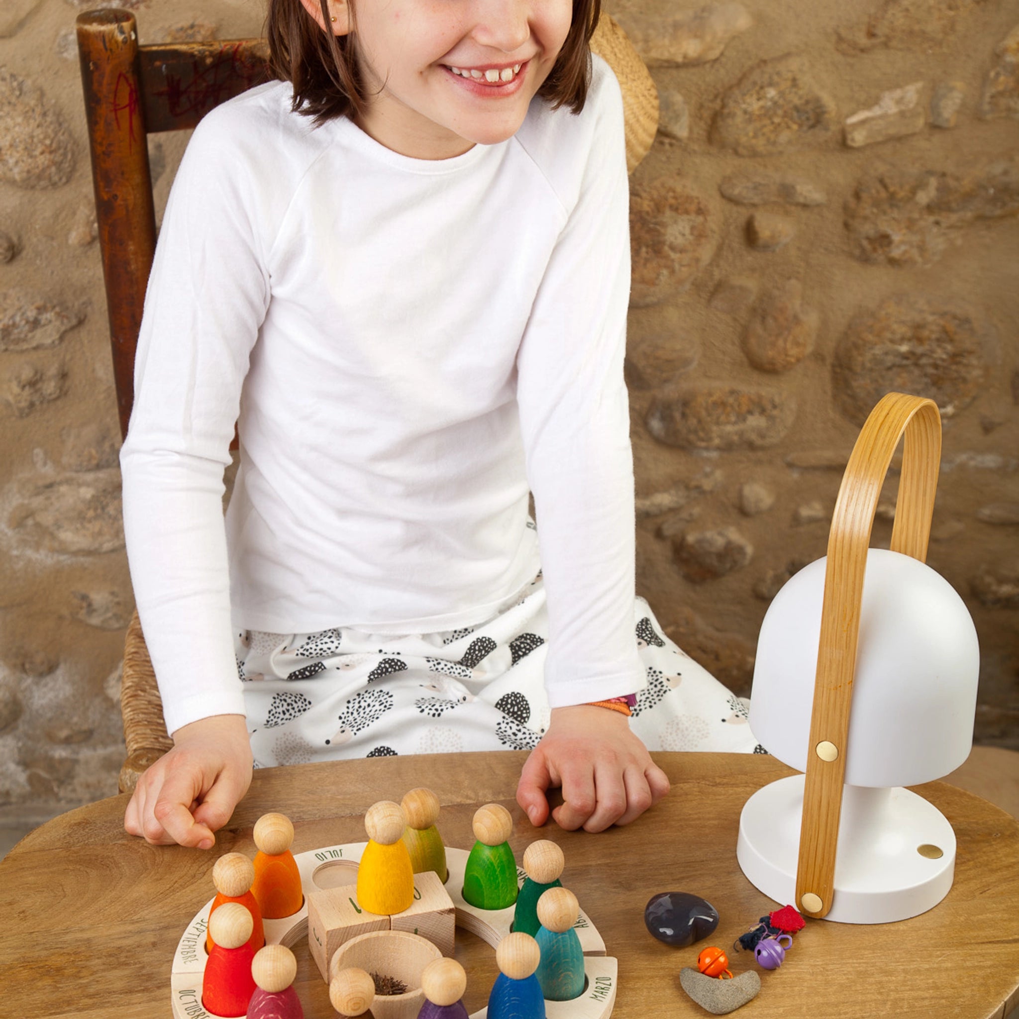 Freies Spiel: Perpetual Calendar aus nachhaltig geforstetem Holz, zeigt ein Mädchen am Tisch mit Holzfiguren und Zubehör wie Tageswürfel und einem Jahreskreis. Fördert das Zeitverständnis.